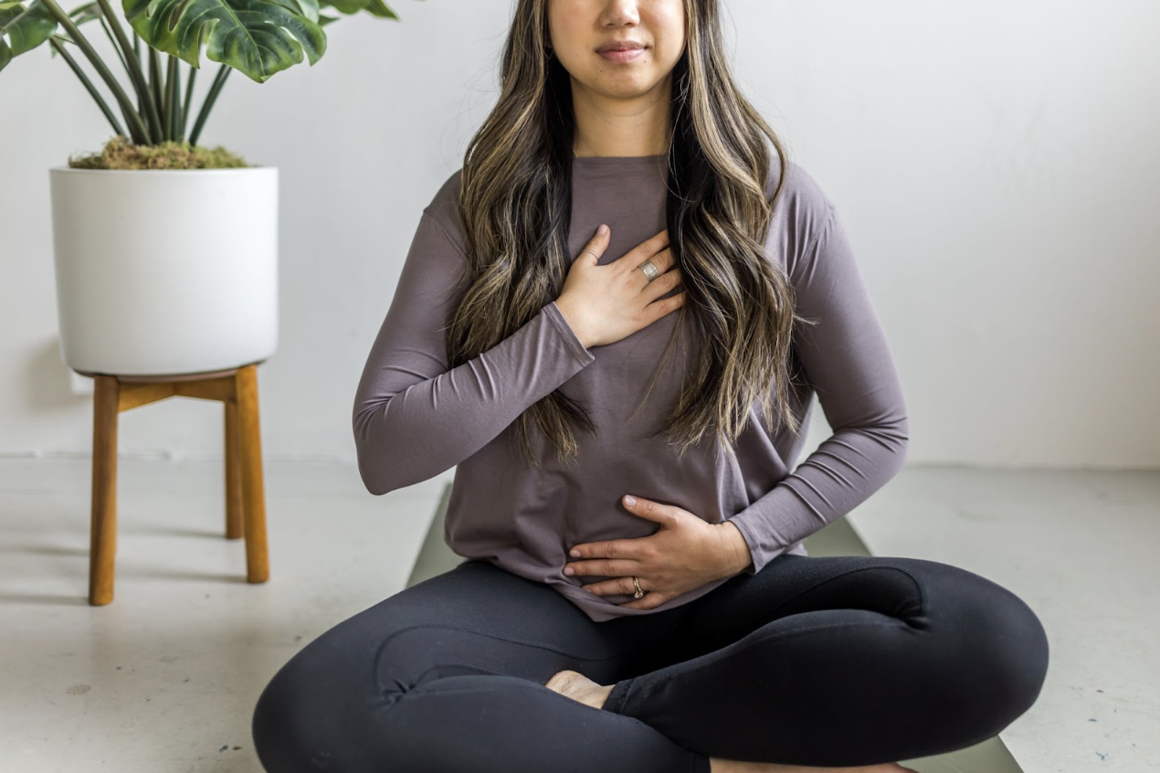 Pelvic Floor Physical Therapist in Boston office sitting on yoga mat with hand on belly and chest.
