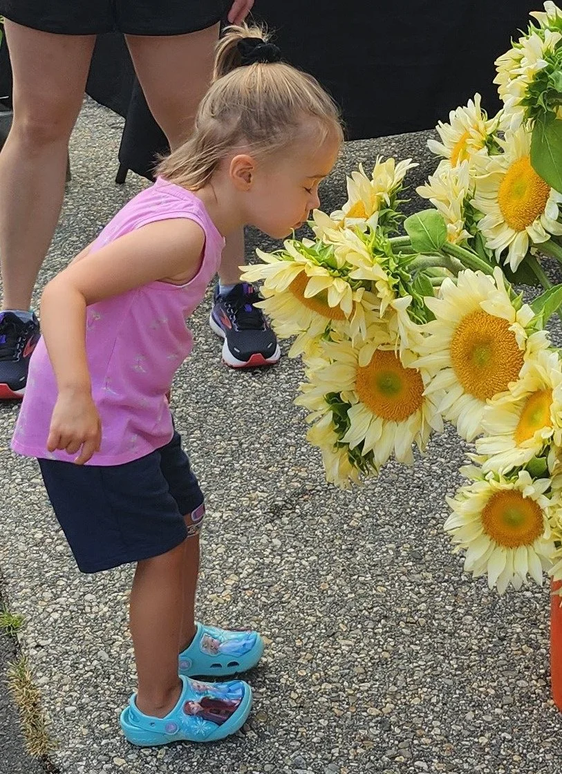 Girl smelling flowers at Blue Back Farmers' Market