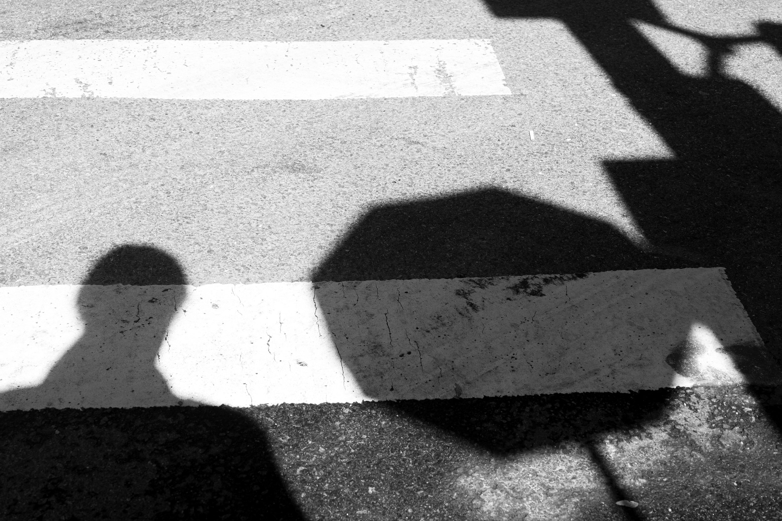 Shadows of a person cast on a crosswalk on the street.