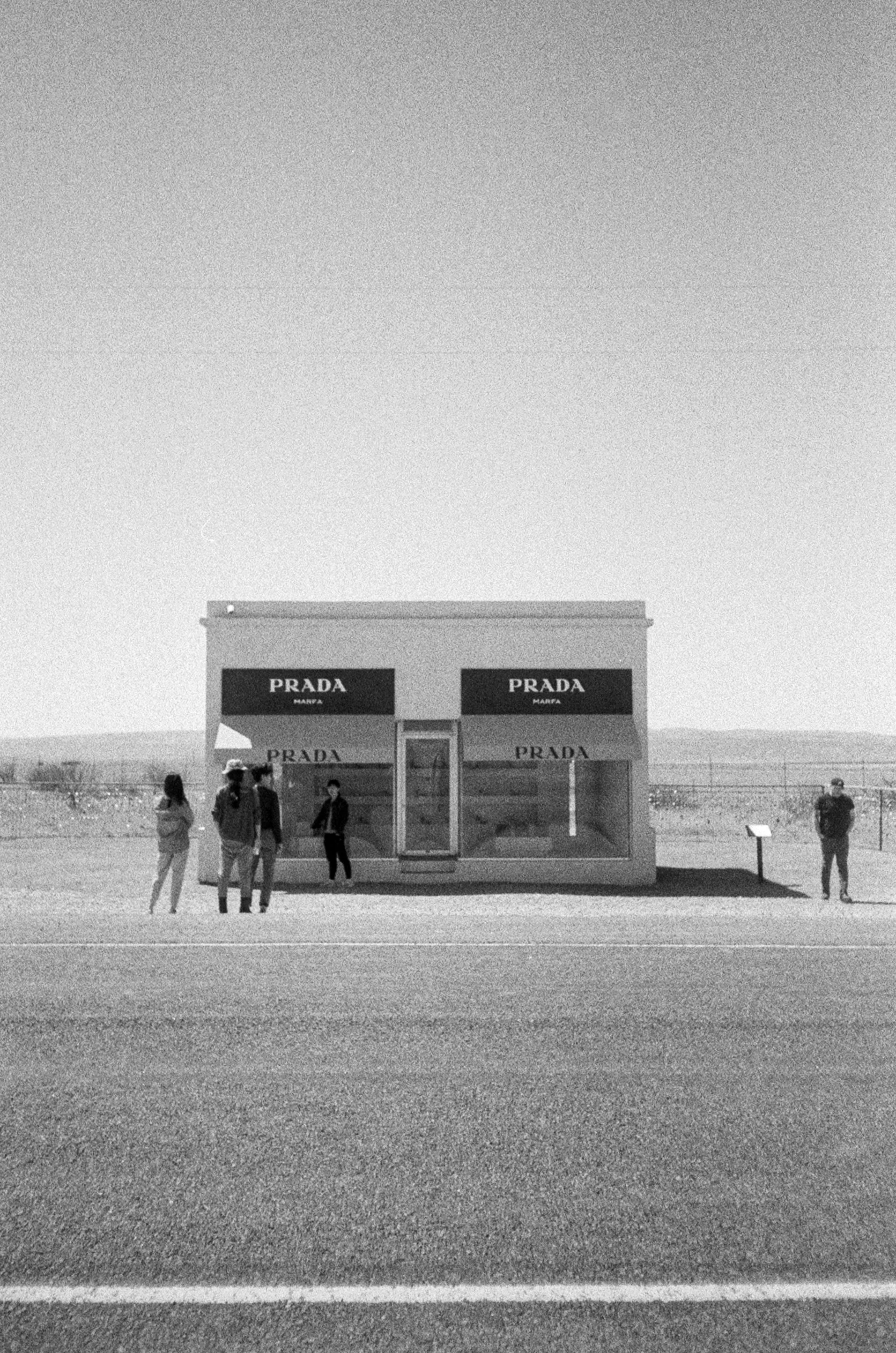 A small Prada store in a remote area with a few people standing outside, under a clear sky.