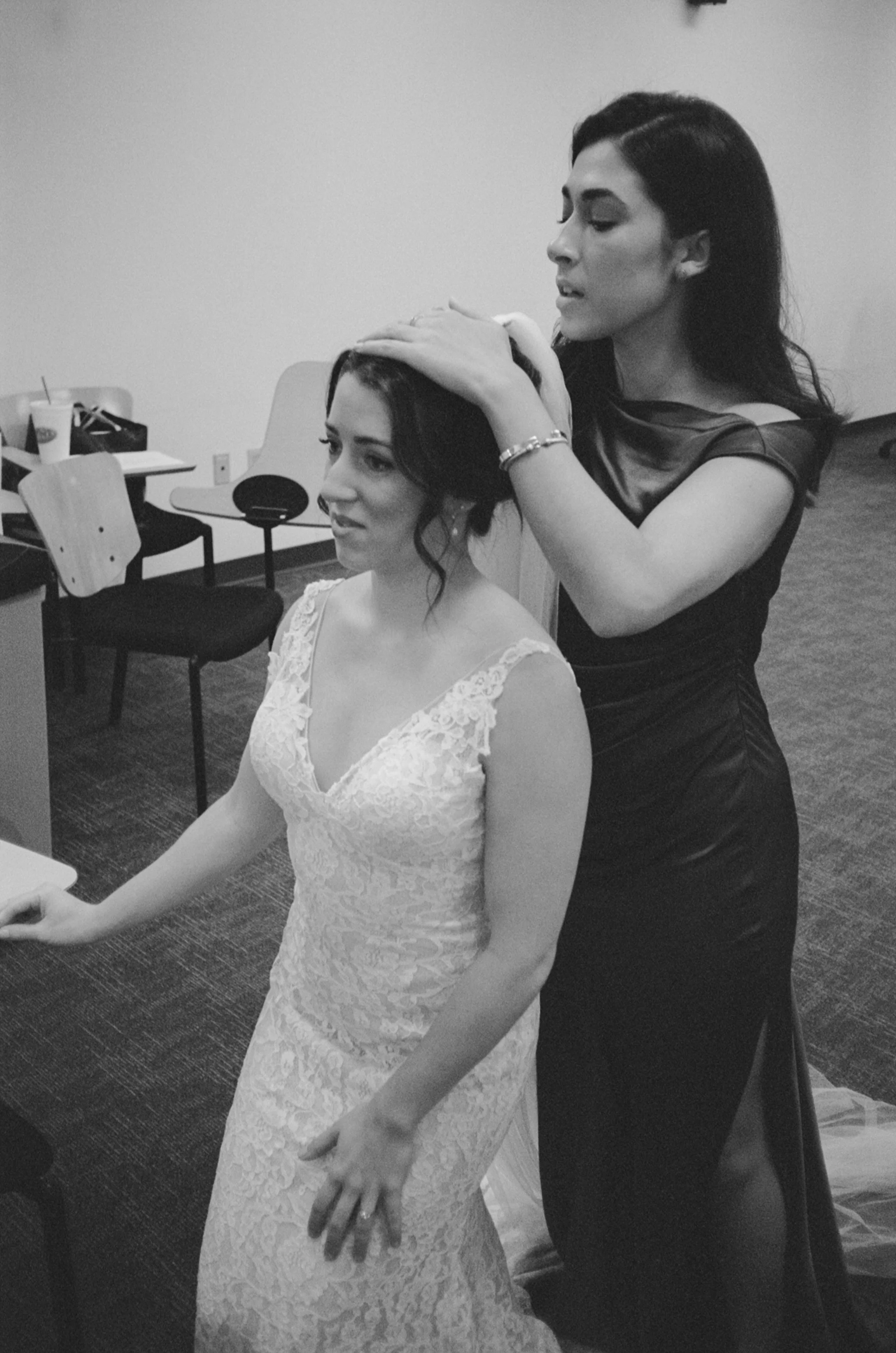A woman in a wedding dress having her hair done by another woman in a dressing room.