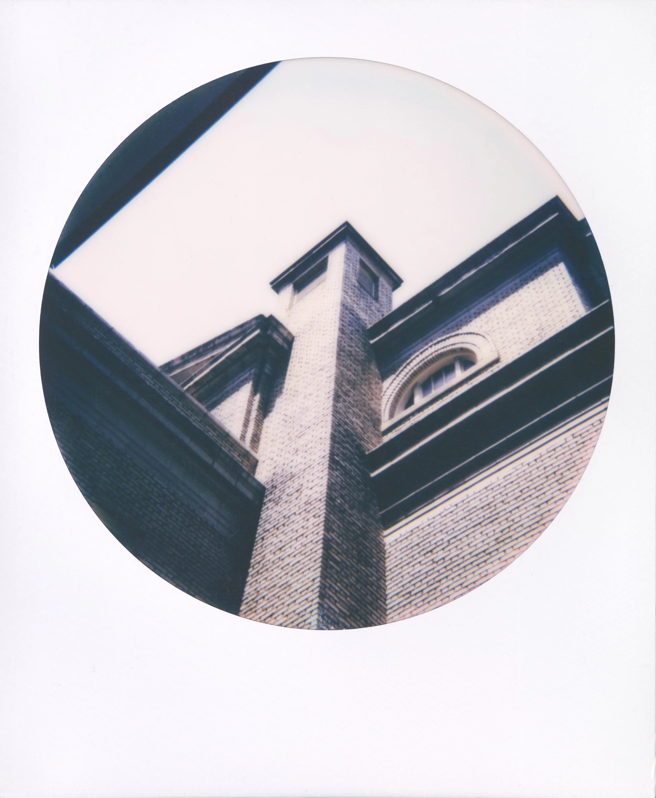 Round-frame polaroid of a low-angle view of a corner of a brick building and arched window.