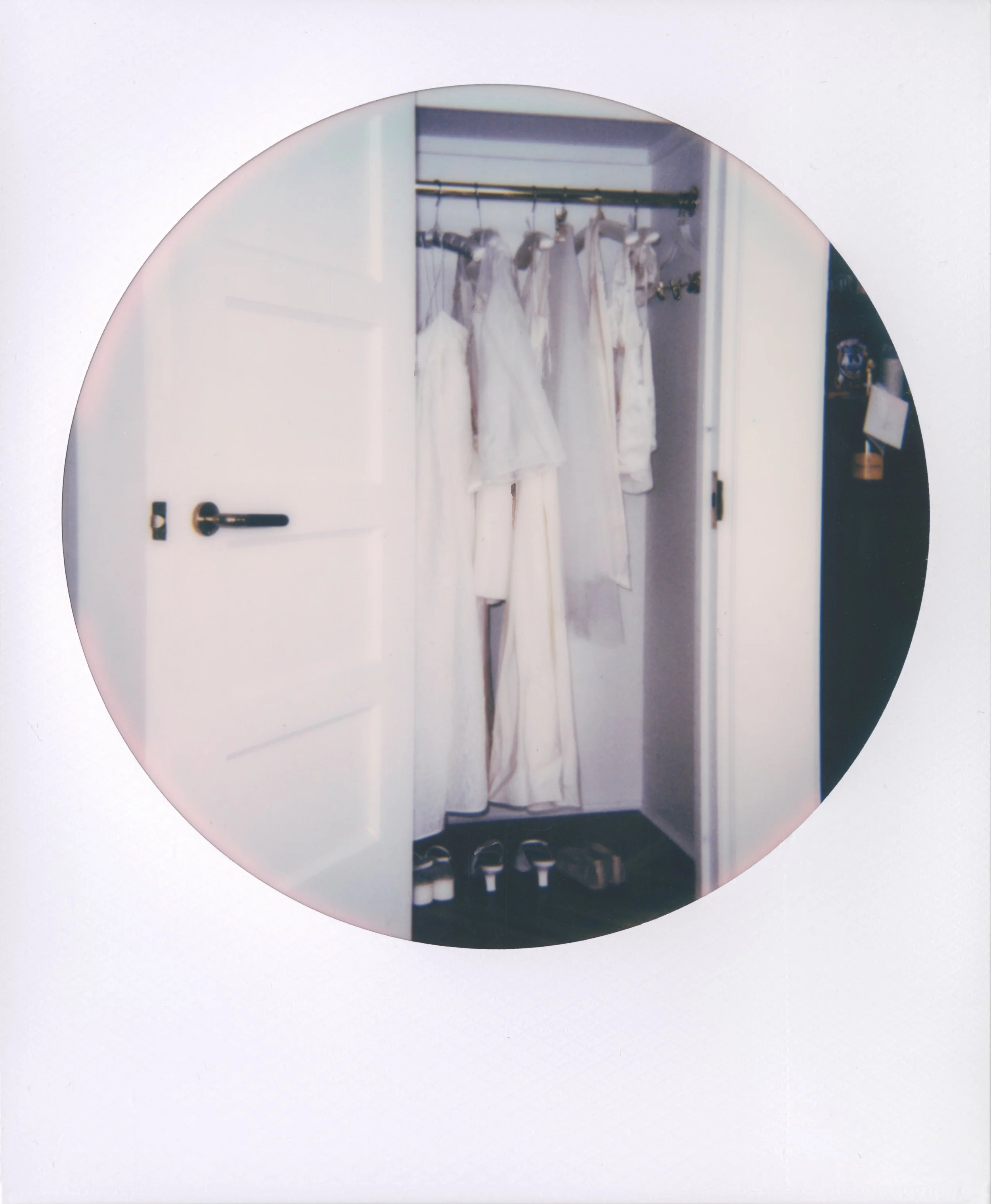 Round-frame polaroid of a closet with white dresses hanging on a gold rod, with shoes neatly arranged below.