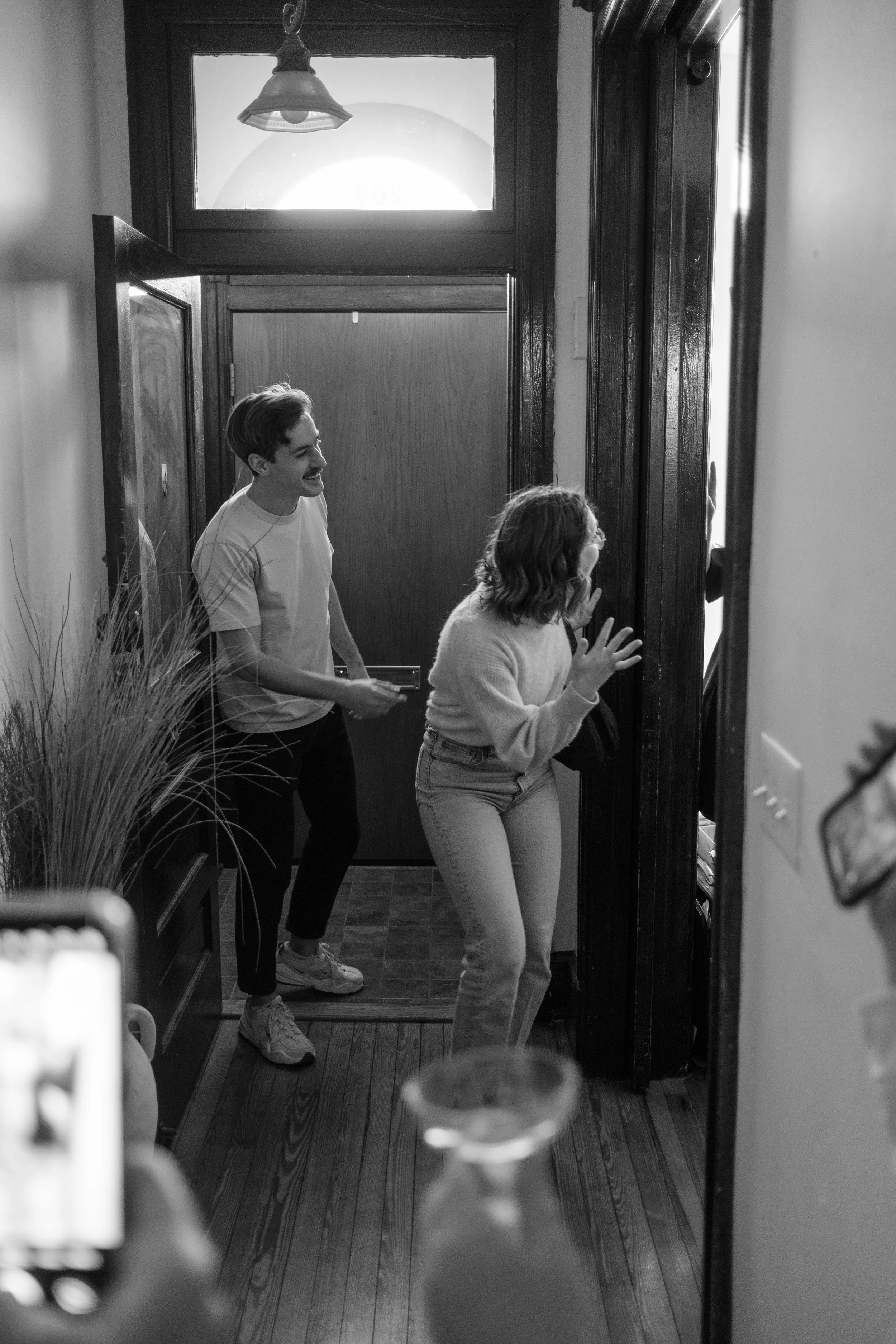 A man and a woman are playfully hiding behind a wall entering inside a house, smiling and laughing.