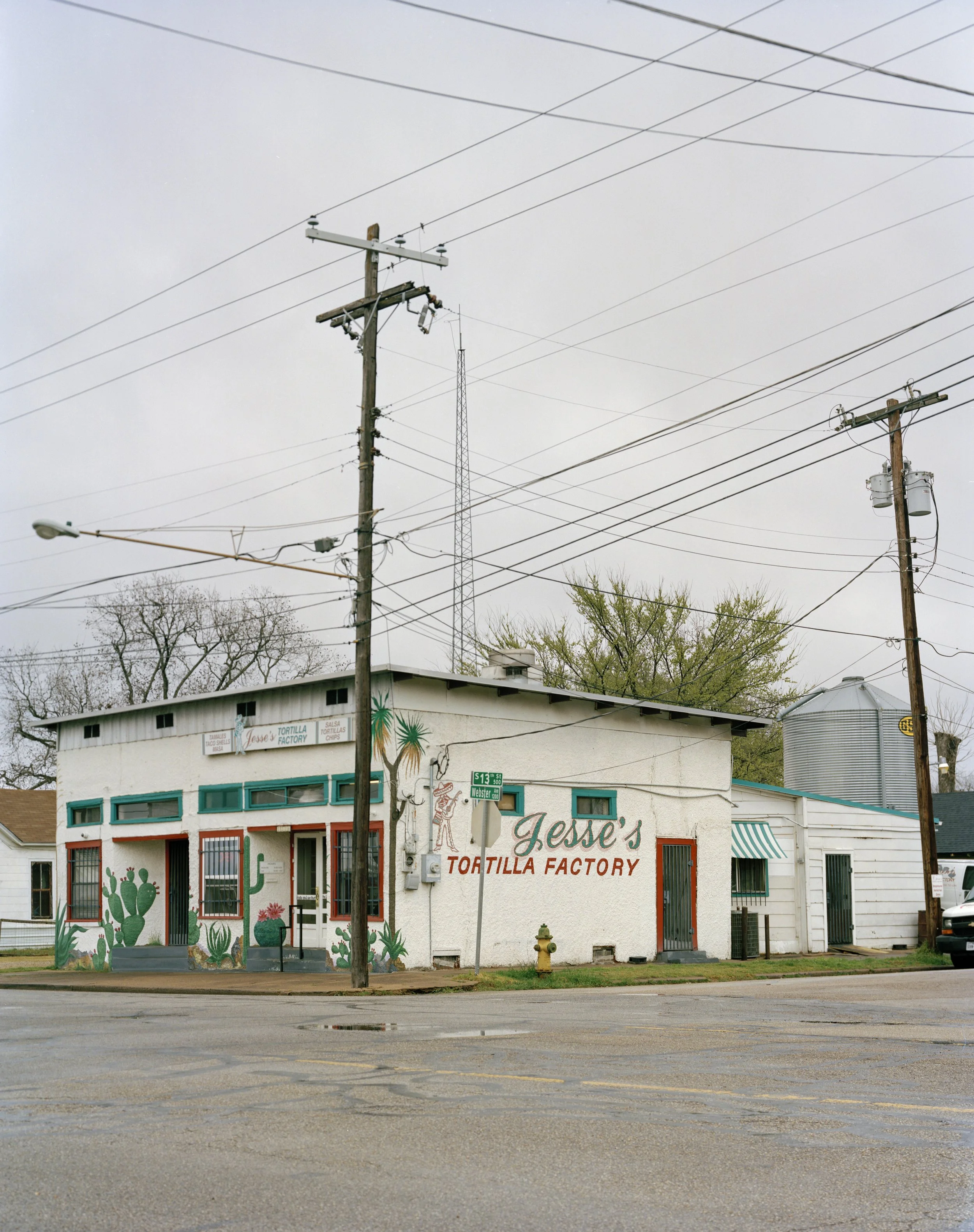 Exterior of Jesse's Tortilla Factory, a small white building with green window trim and desert-themed cactus murals.