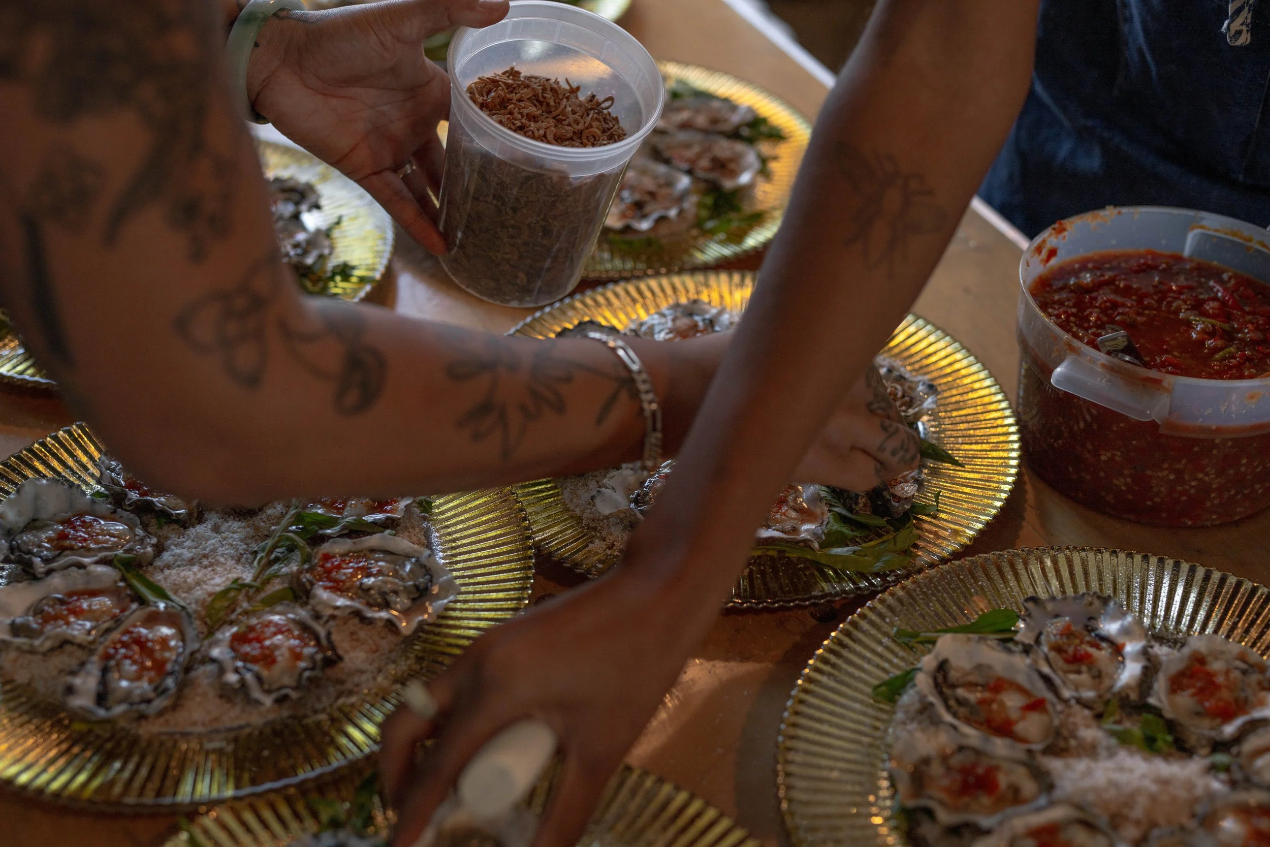 Hands of people preparing and serving oysters on golden trays.