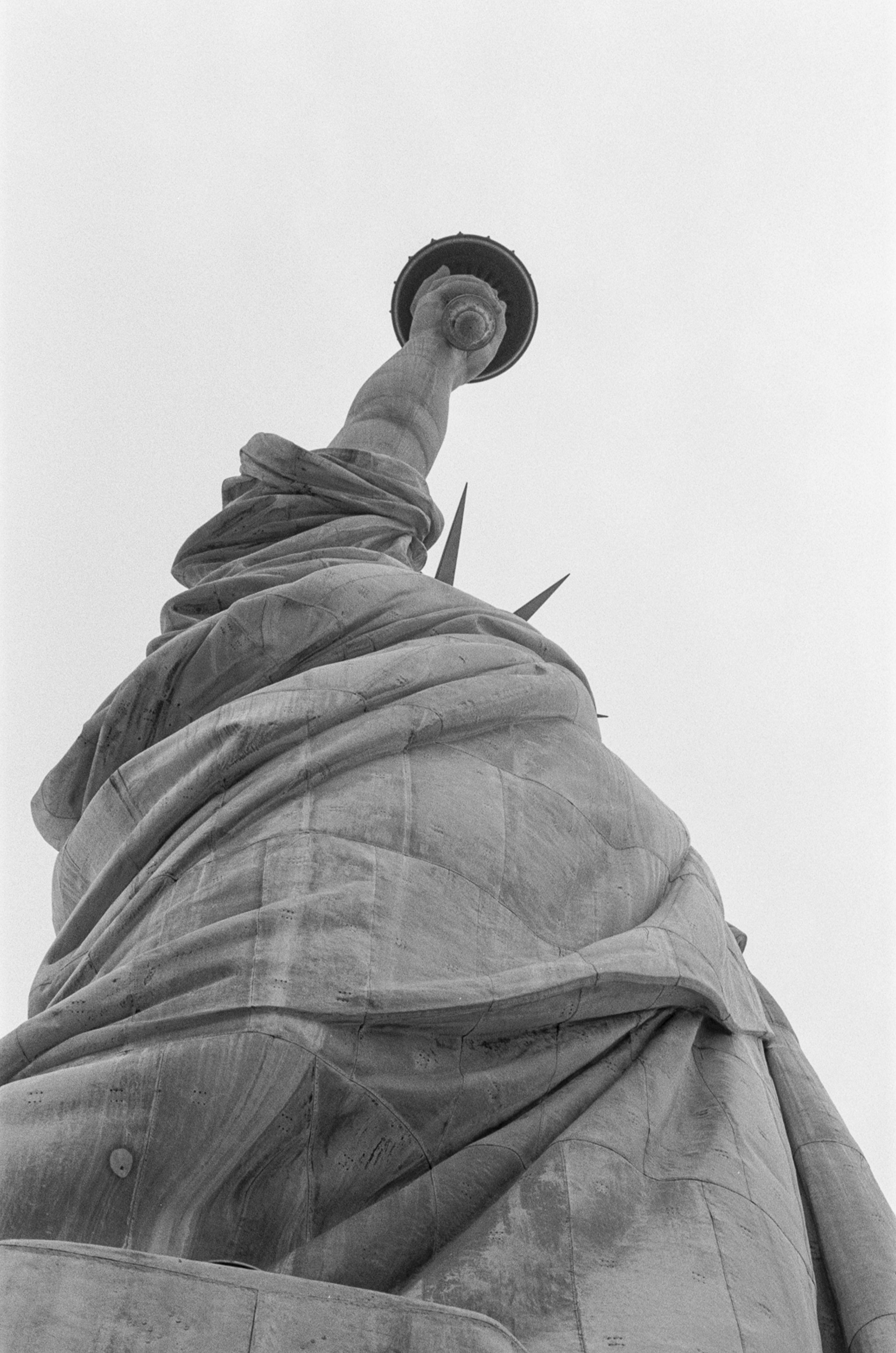 Black and white photo of the Statue of Liberty taken from below, showing the torch held high above the head.