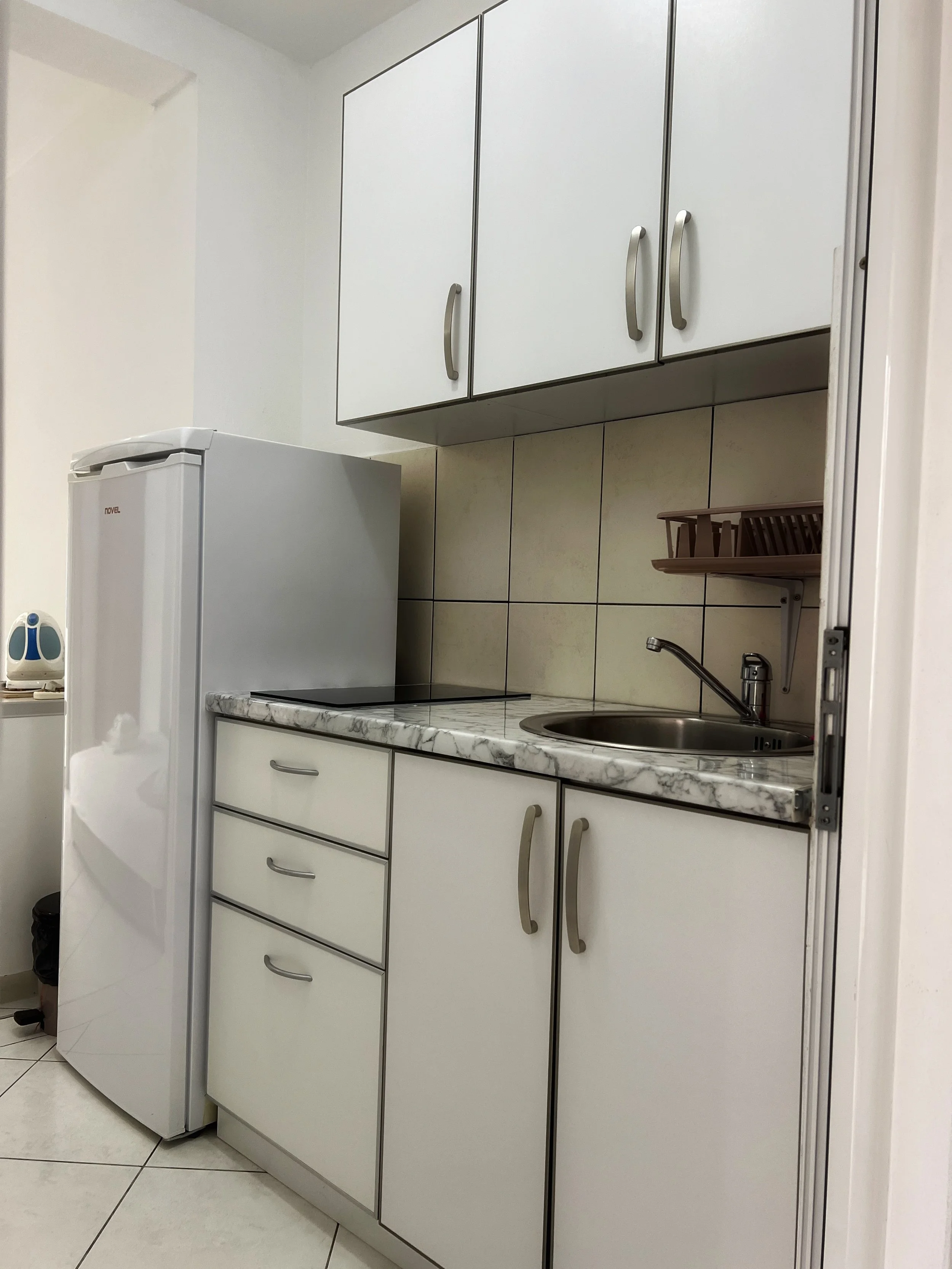 Small kitchen with white cabinets, a marble countertop, a small sink, and a refrigerator.