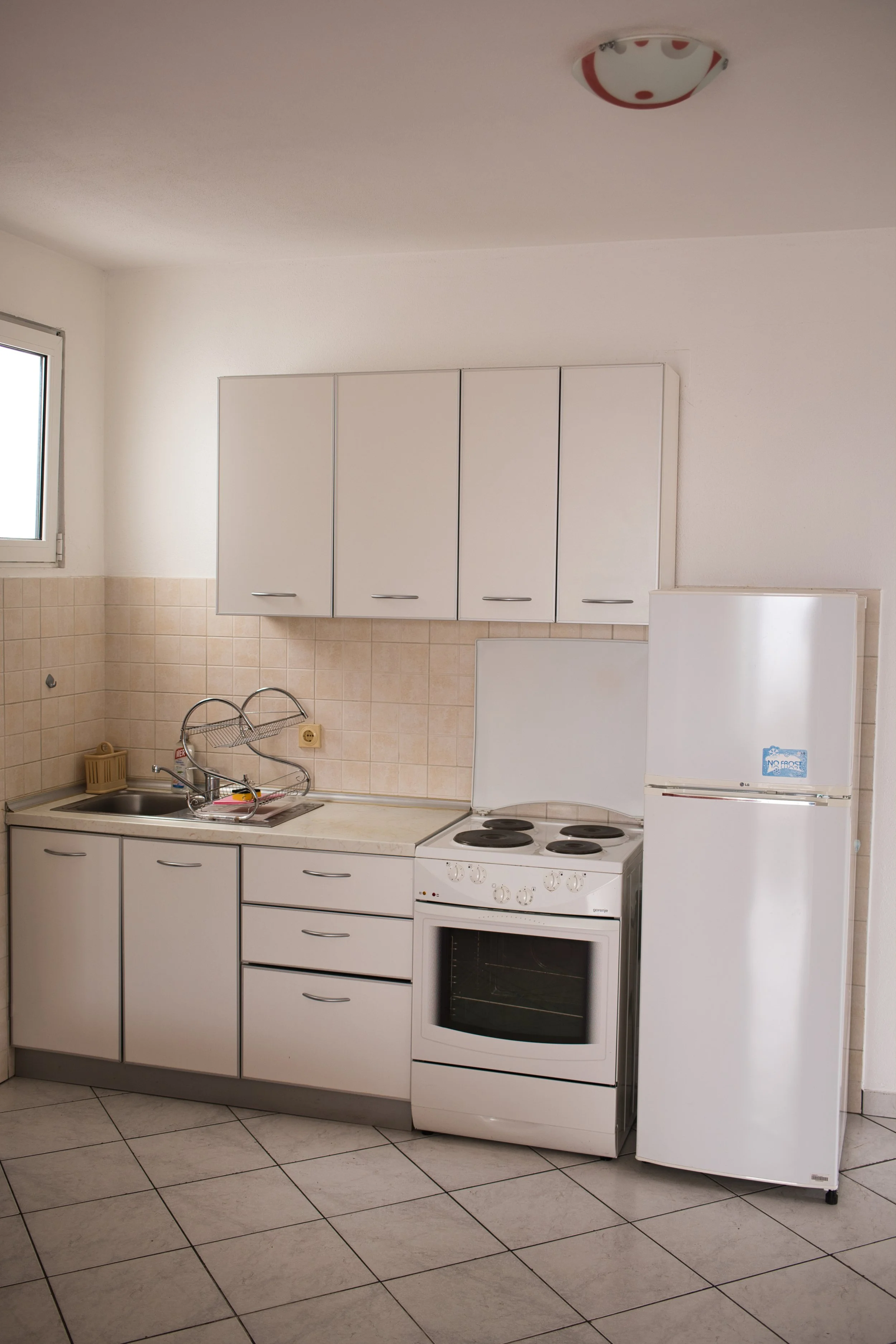 Small kitchen with white cabinets, beige tiled wall, small sink, electric stove, and refrigerator.