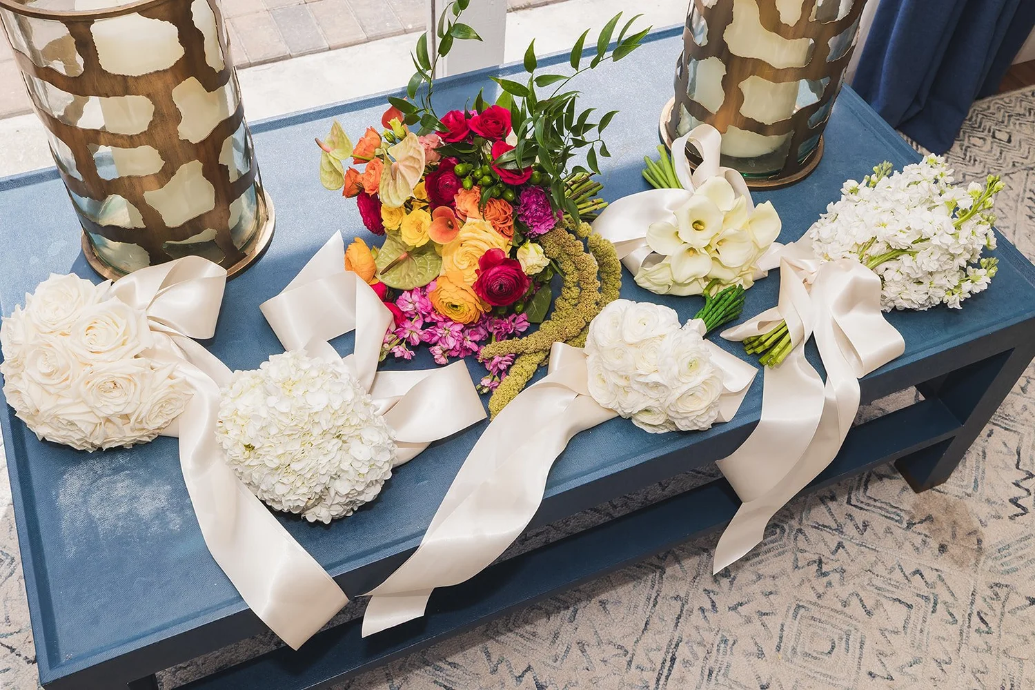 Karolina's bouquet of pink, orange and yellow blooms beside white bouquets tied with ivory ribbon on a blue table at Seabrook Island Club on Seabrook Island, South Carolina.