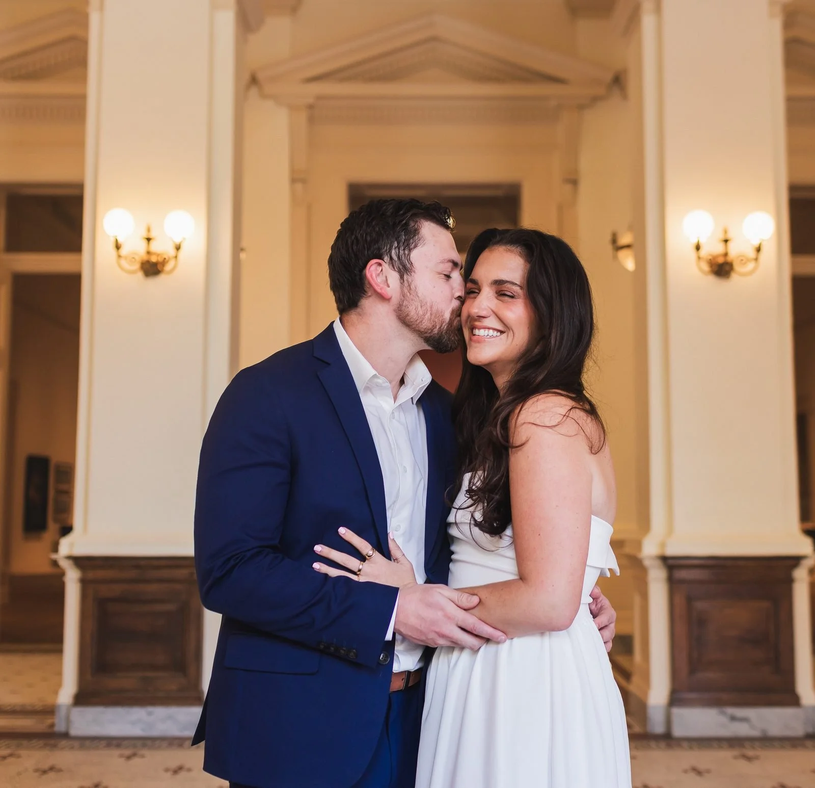 Man kissing his fiancee's cheek between white columns at the Gibbes Museum of Art in Charleston