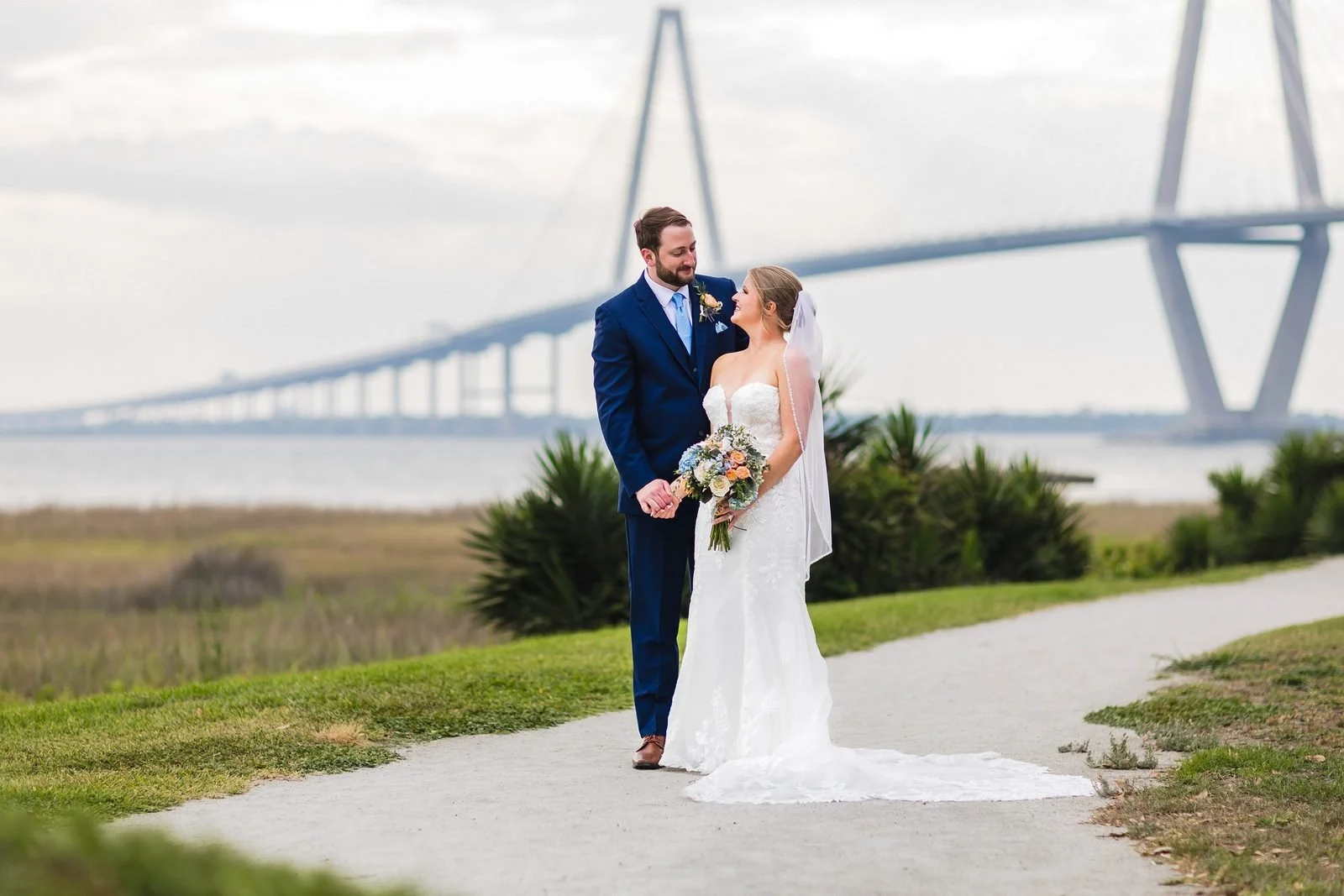 Close portrait of a bride and groom with her bouquet, the Ravenel Bridge towers soft behind them in Charleston