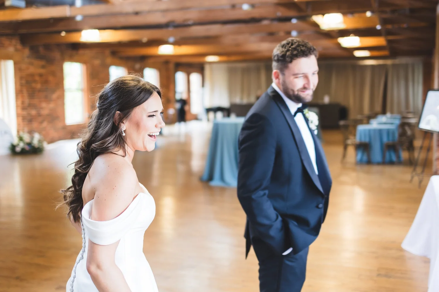 Madison and Derek together in the Huguenot Mill reception hall, with exposed brick and timber behind them, in Greenville, South Carolina.