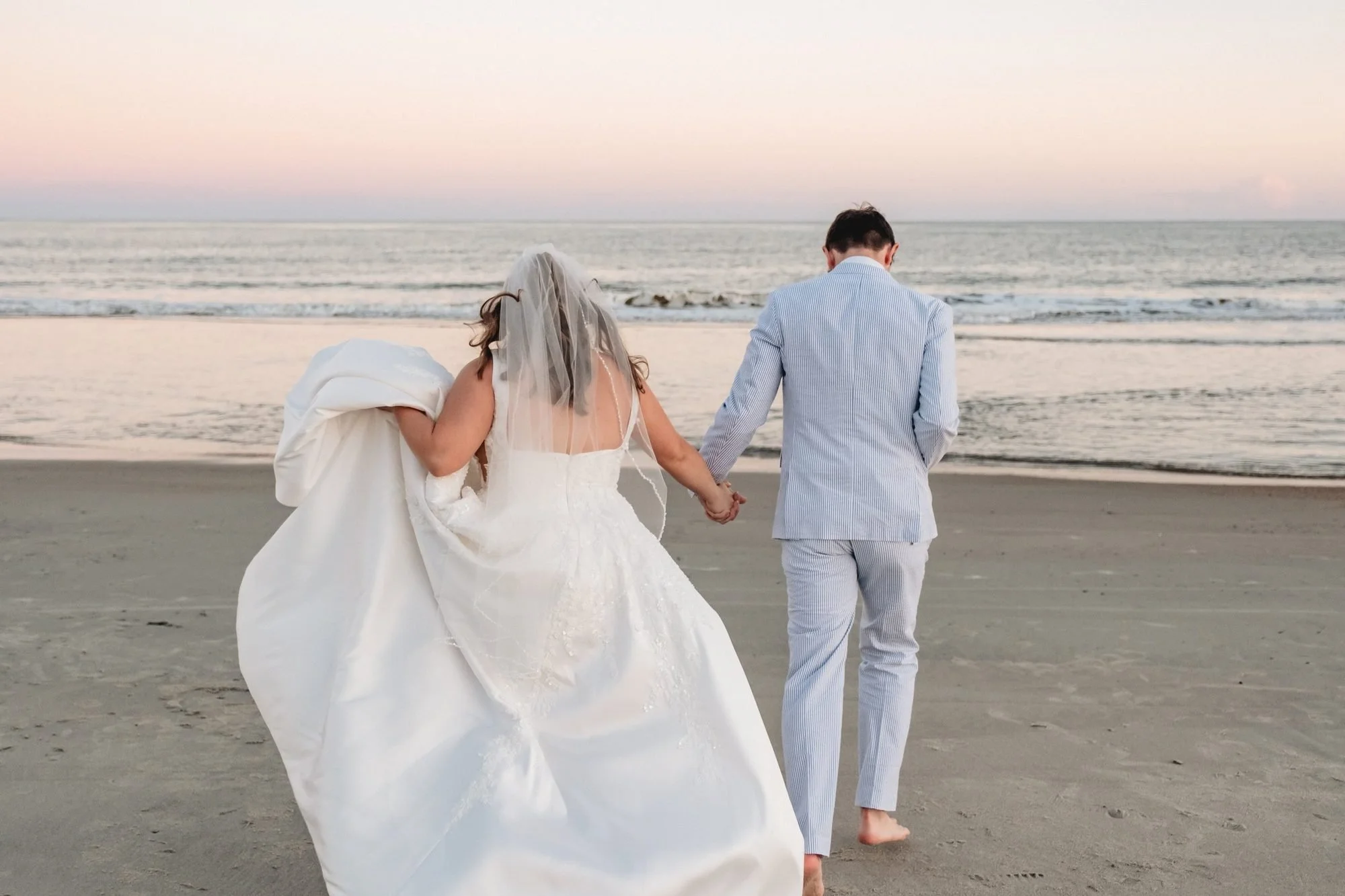 Bride and groom walking on the beach at sunset