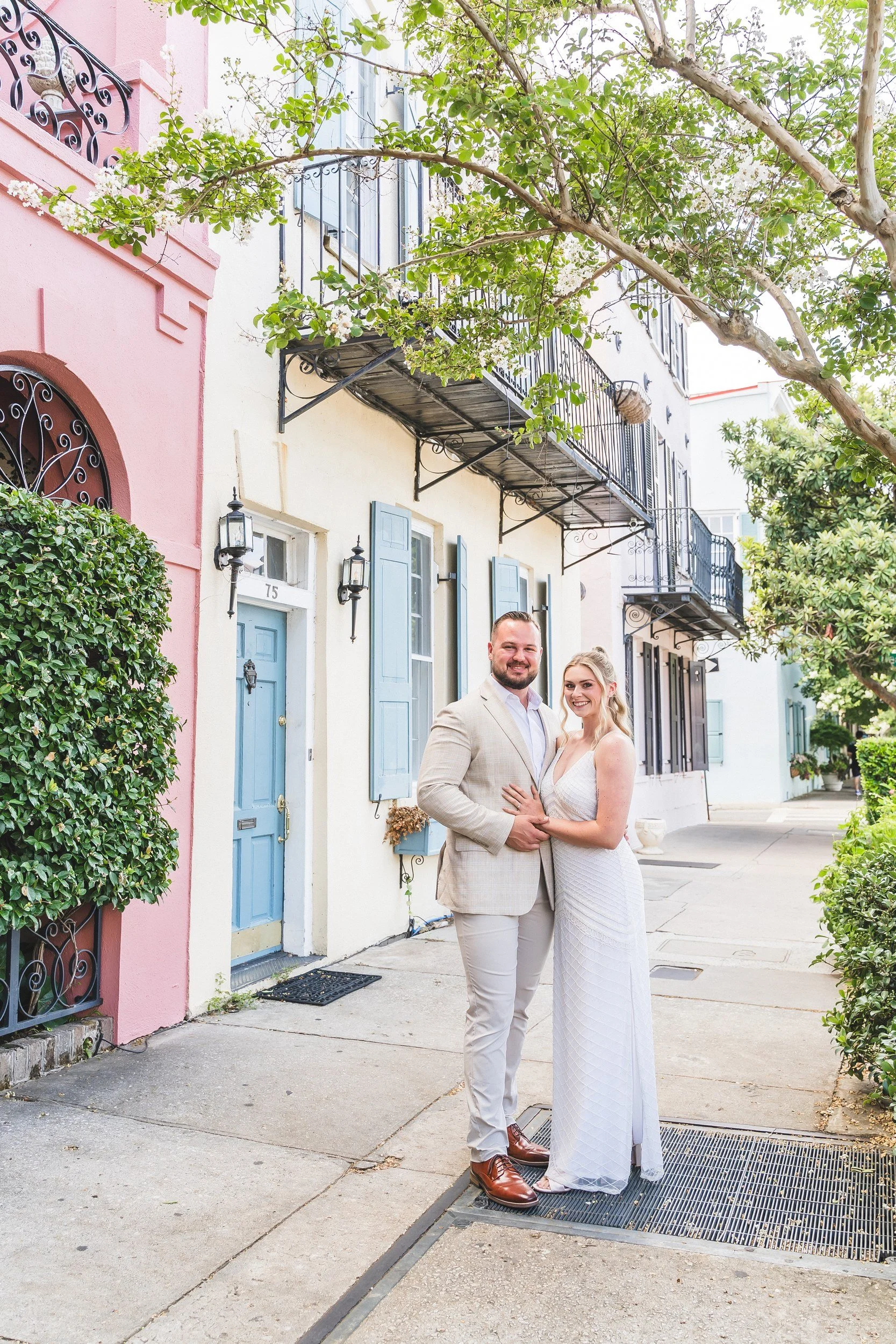 Engaged couple embracing by a pink house on Rainbow Row, Charleston