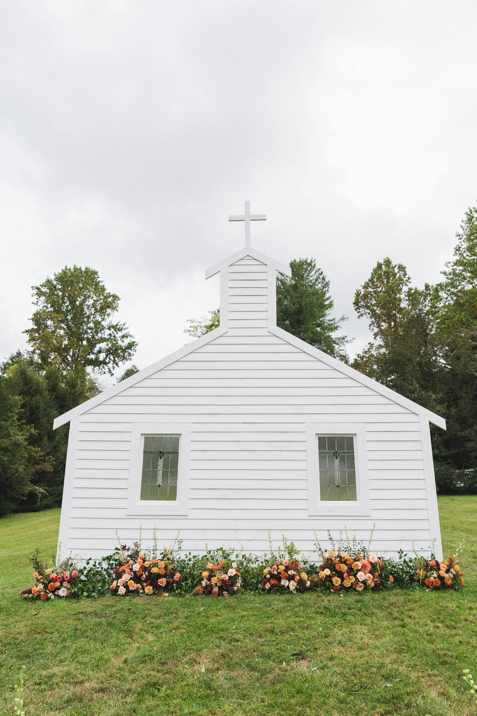Aisling and Neal's wedding in Flat Rock, North Carolina. A white chapel with a cross and orange and pink flowers.