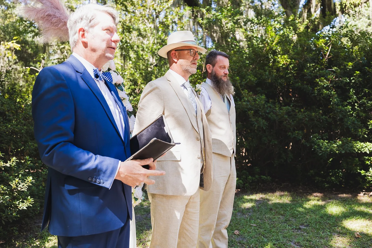 Markus waits at the front of the ceremony beside the officiant and a groomsman, with live oaks and Spanish moss behind them, at Wicklow Hall in Georgetown, South Carolina.