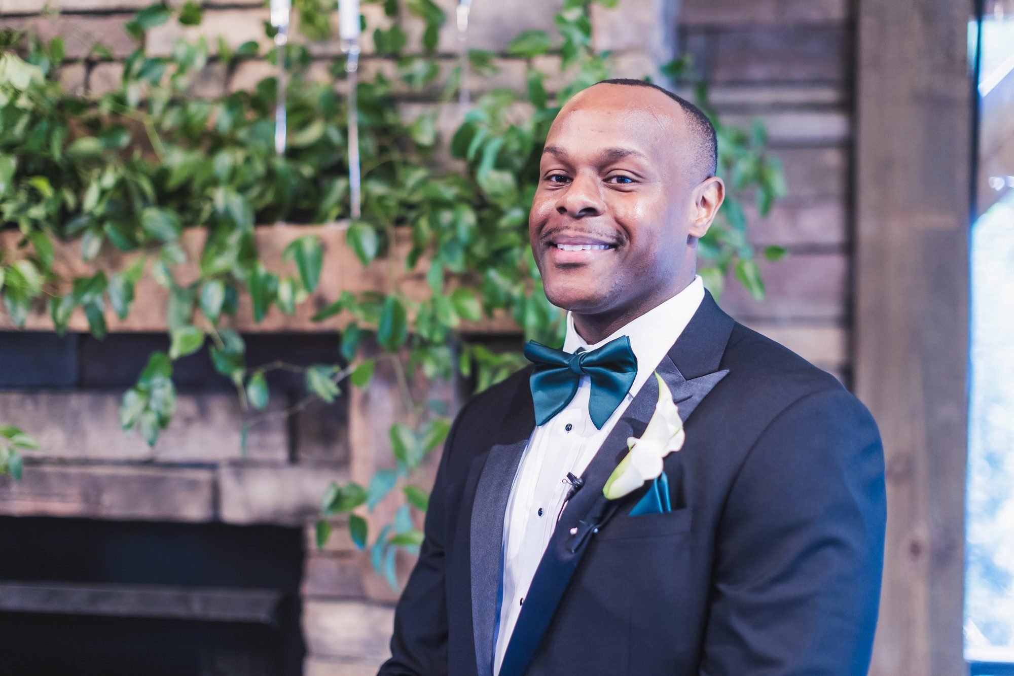 Ashlee and Chris wedding at Southern Oaks Event Venue in Gilbert, South Carolina: groom smiling at the altar with greenery behind him.