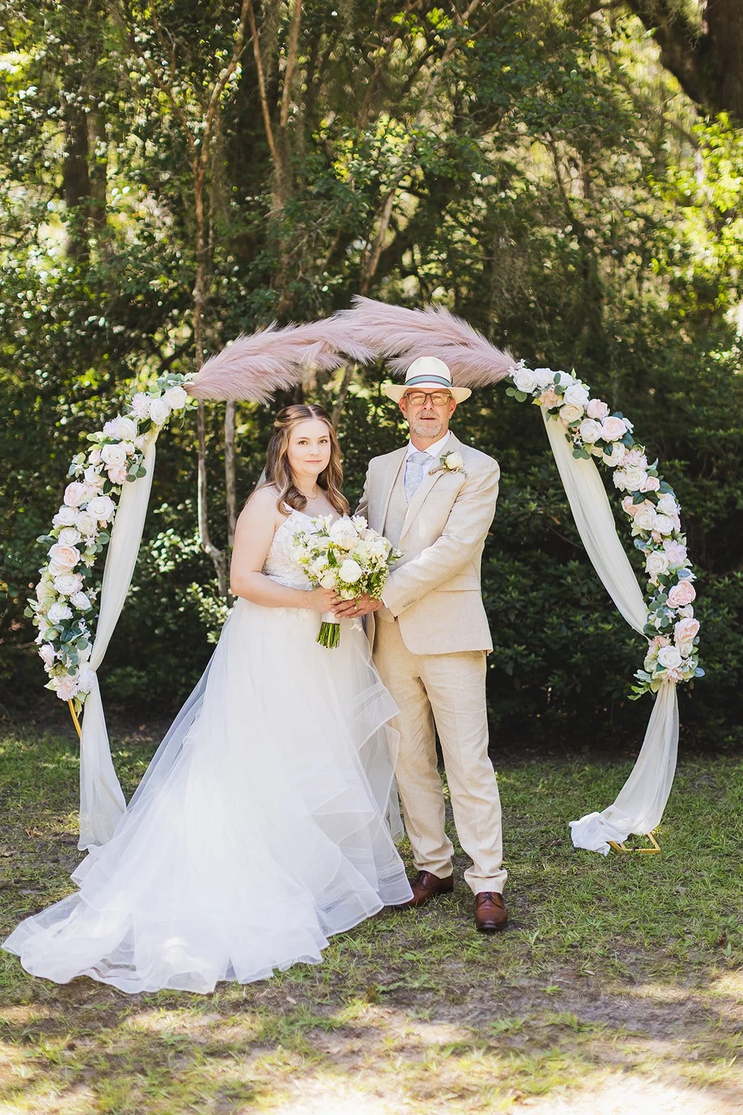 Sarah and Markus stand together at their floral ceremony arch on the lawn at Wicklow Hall in Georgetown, South Carolina.