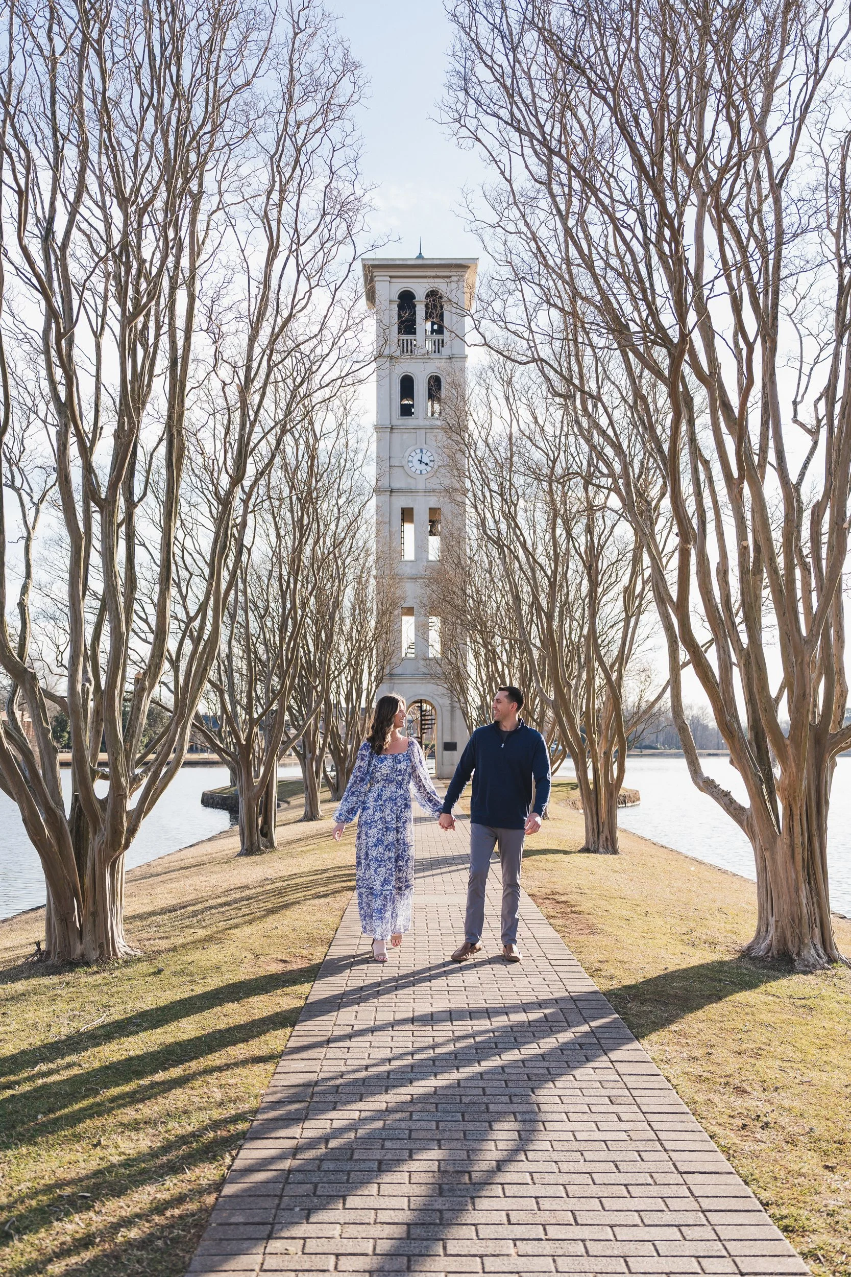 Couple holding hands on brick path with clock tower