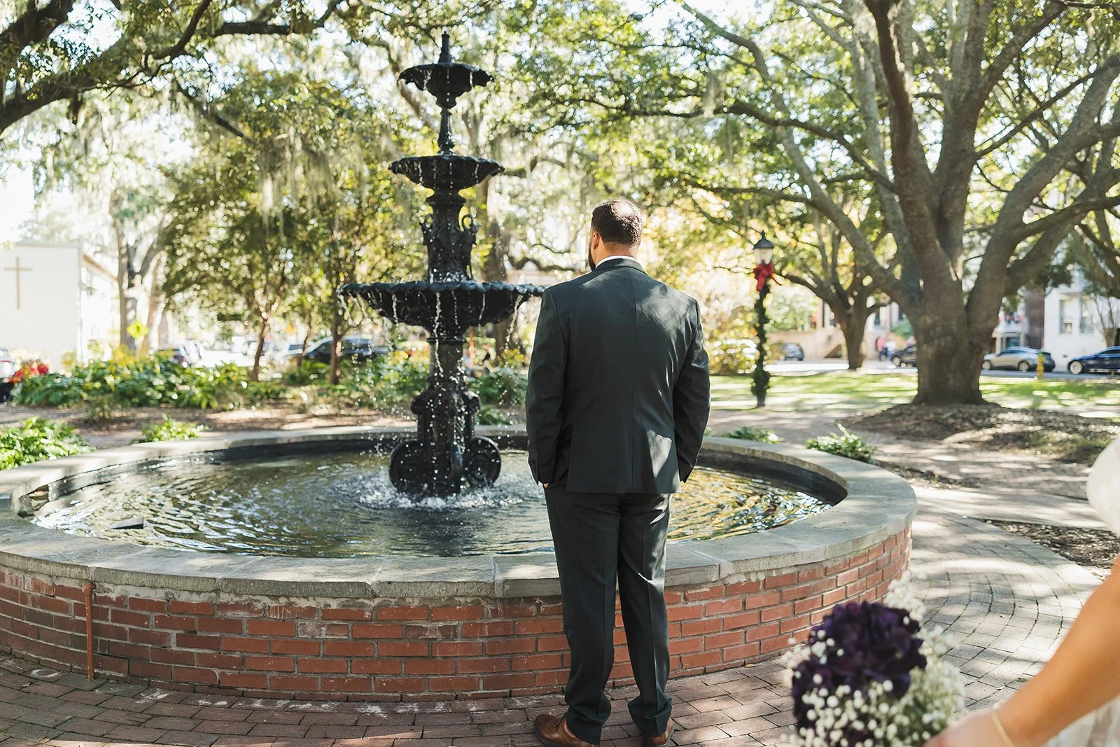 Groom waits by a fountain under Spanish moss in Savannah's historic district before the first look
