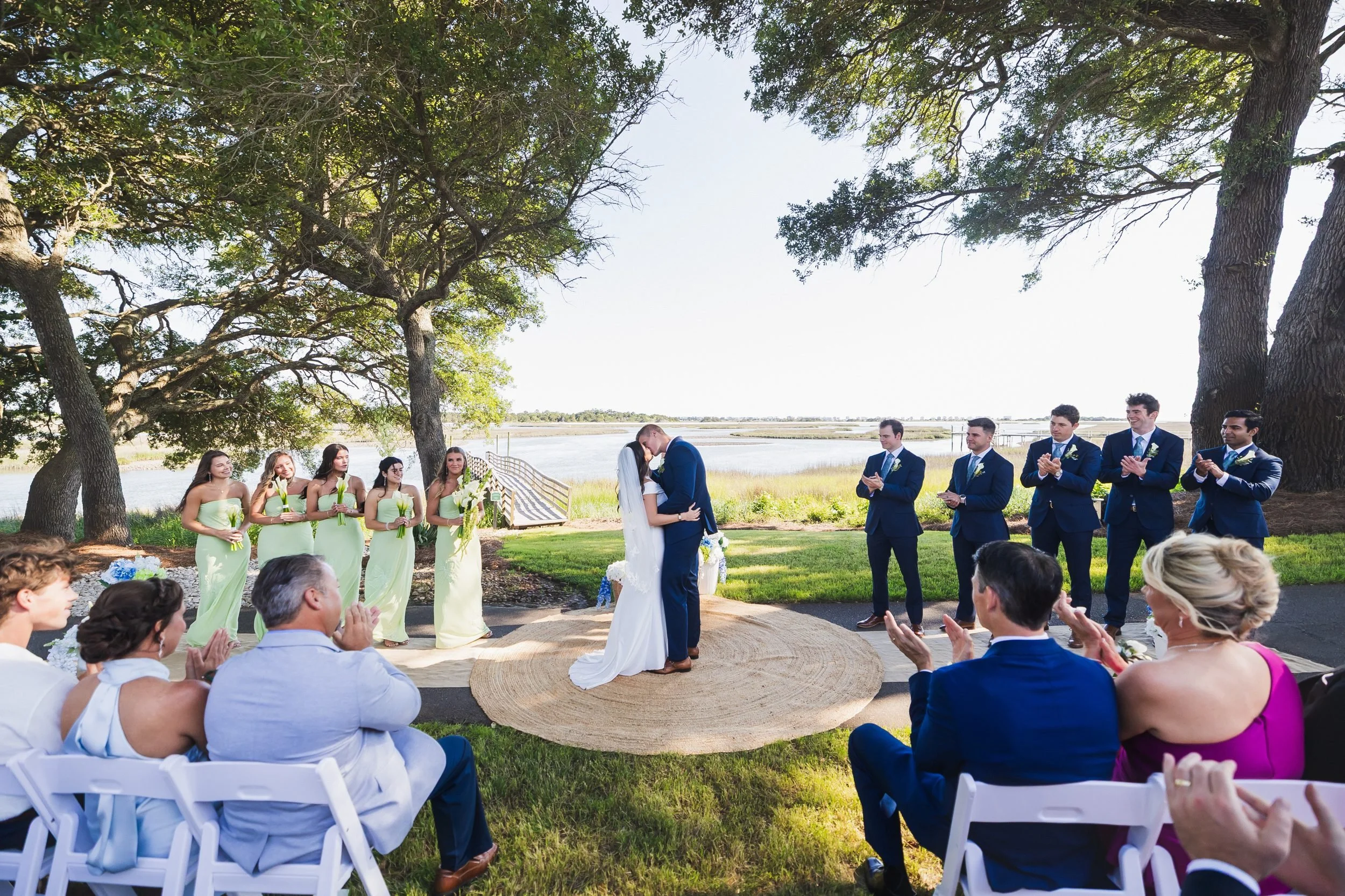 Payton and Ryan's wedding at Lockwood Folly Country Club in Holden Beach, North Carolina. Their first kiss as the wedding party claps.
