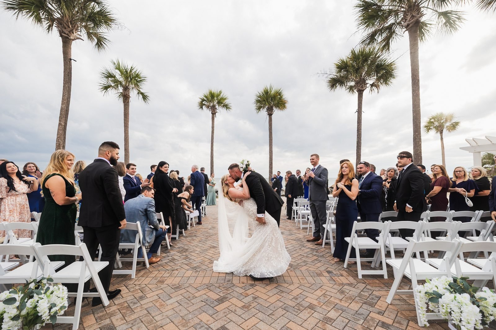 Groom dipping the bride for a kiss down a palm-lined aisle as guests cheer at a Seabrook Island wedding