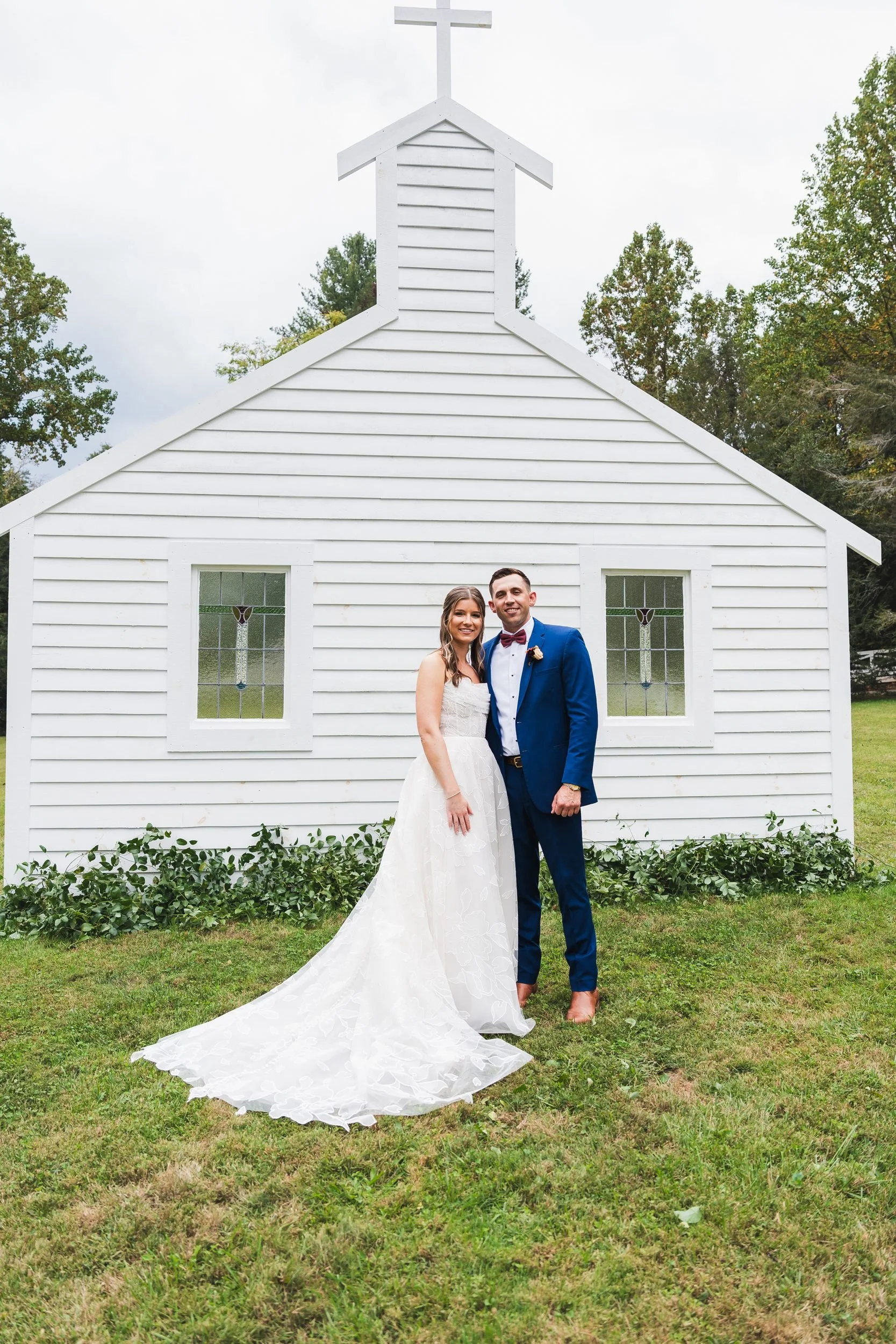 Aisling and Neal's wedding in Flat Rock, North Carolina. The couple poses in front of a white chapel, the groom in a royal-blue suit.