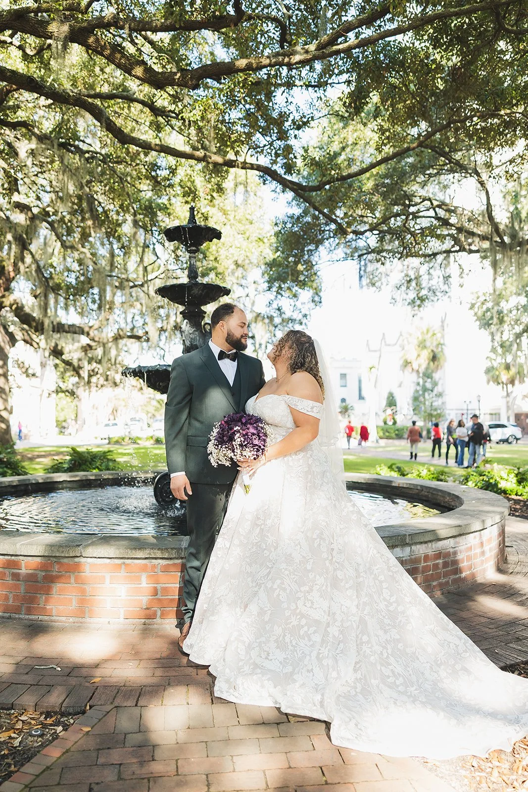 Bride and groom walk past a fountain beneath Spanish moss in Savannah's historic district
