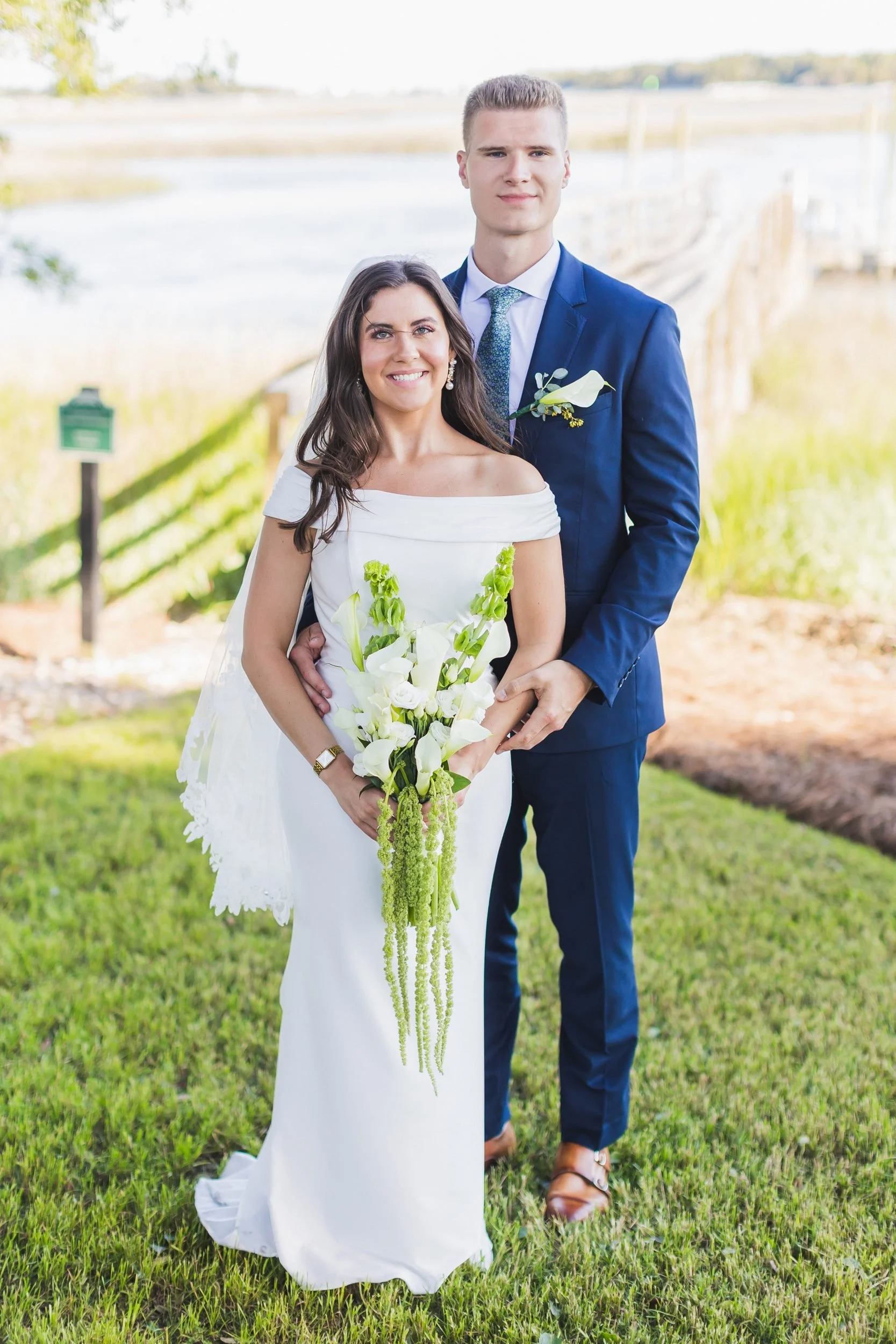 Payton and Ryan's wedding at Lockwood Folly Country Club in Holden Beach, North Carolina. The bride smiles with a calla lily bouquet, the marsh behind her.