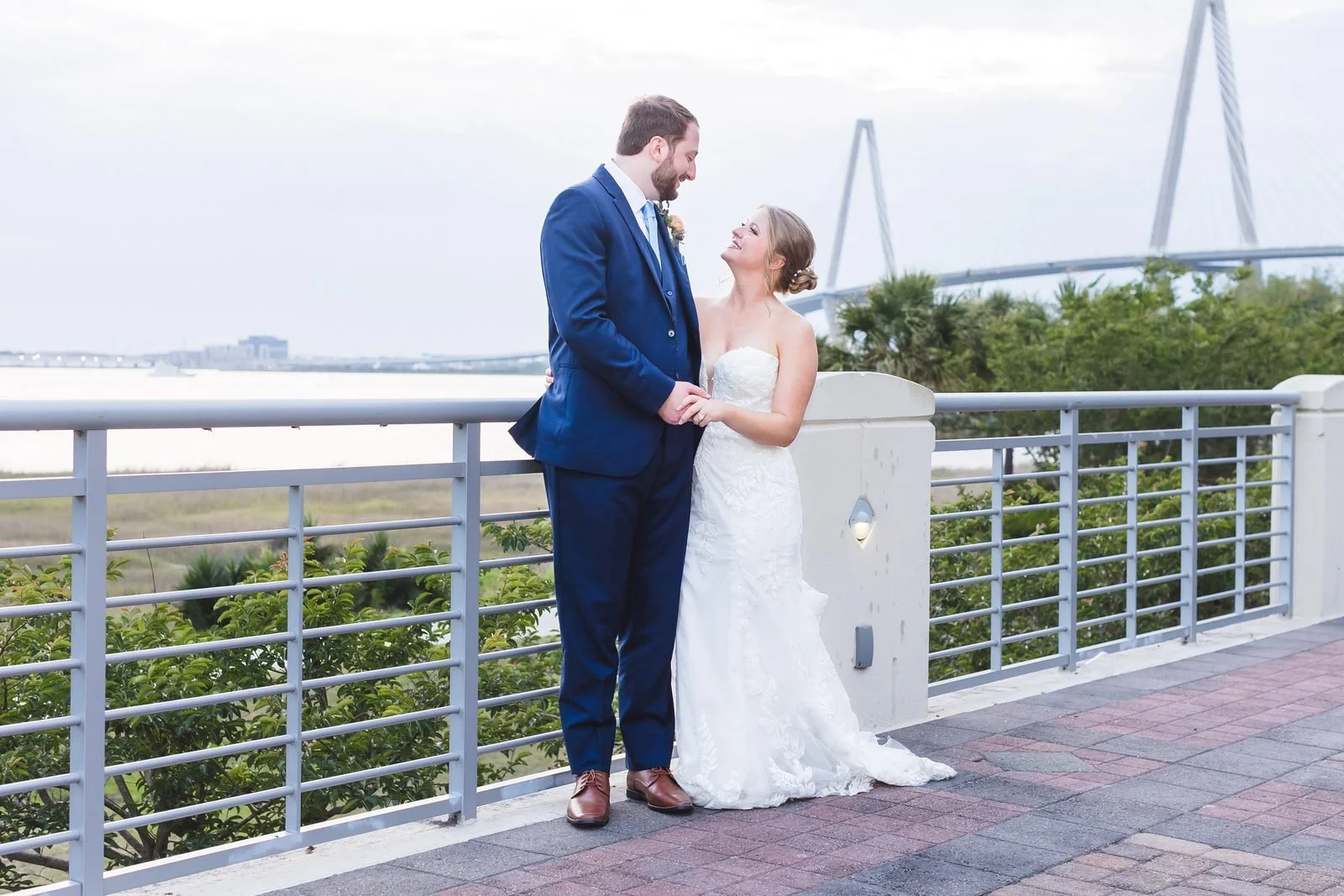 Bride and groom gazing at each other at a waterfront railing in Charleston with the Ravenel Bridge at right