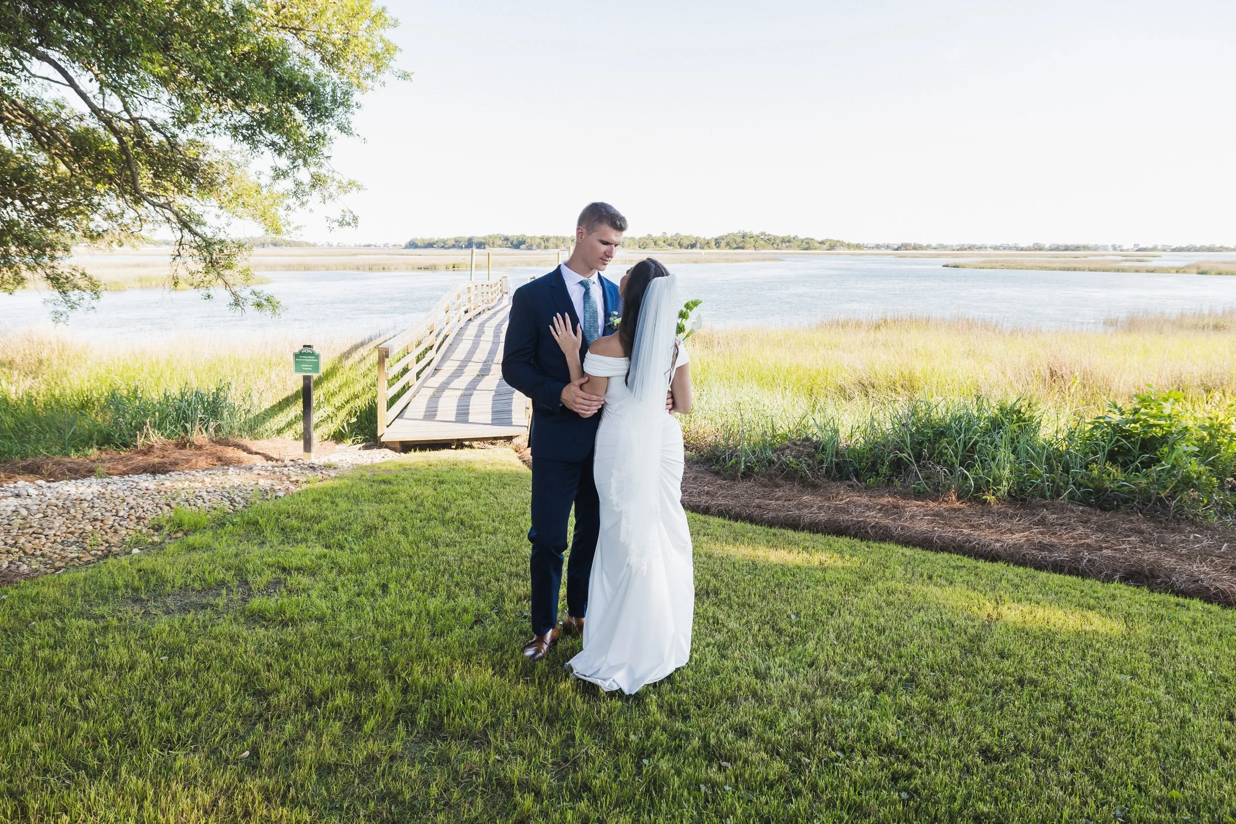 Payton and Ryan's wedding at Lockwood Folly Country Club in Holden Beach, North Carolina. The couple embraces on the lawn by the marsh and live oaks.
