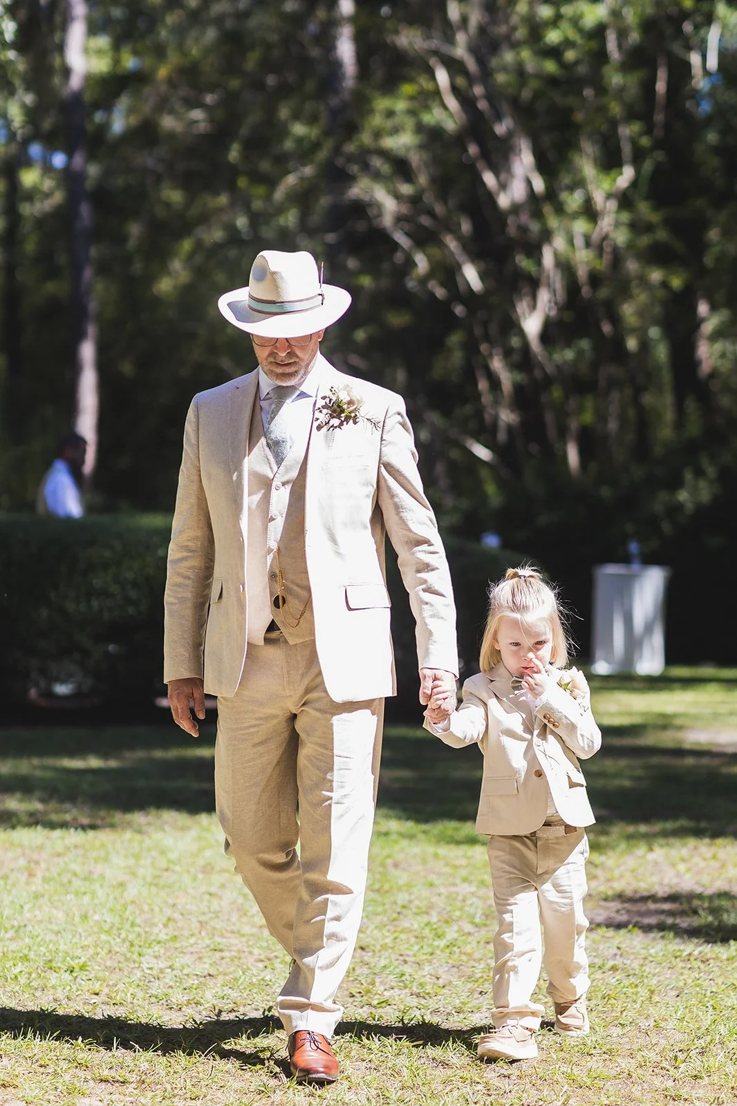 Markus walks down the aisle hand in hand with a little one in a matching cream suit at Wicklow Hall in Georgetown, South Carolina.