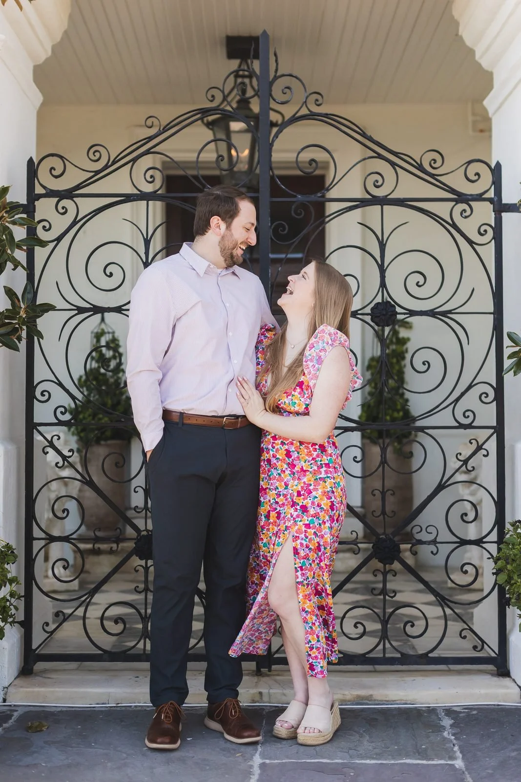 Engaged couple laughing in front of an ornate wrought-iron gate in downtown Charleston