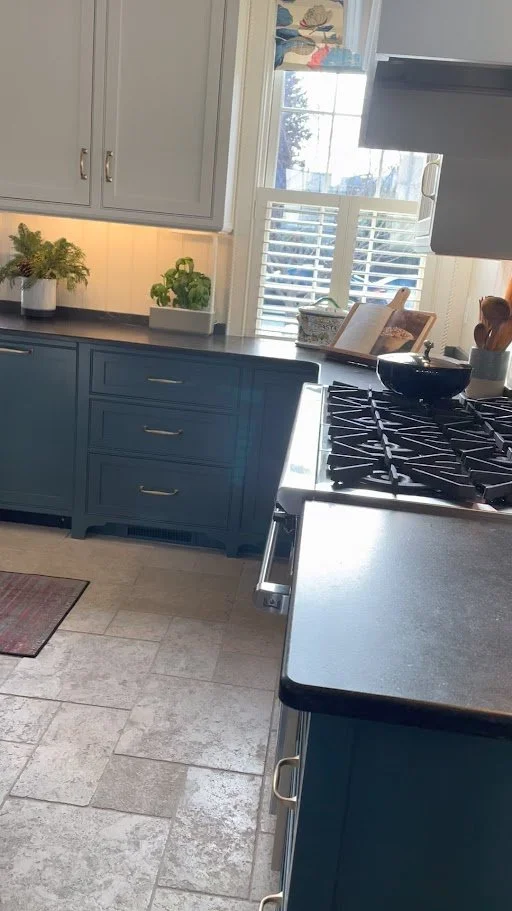Kitchen with blue cabinets, a window with white blinds, and a gas stove with a black pot on top.