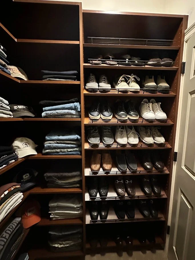 Wooden shoe rack filled with various casual and formal shoes, alongside shelves with folded clothing, in a closet setting.