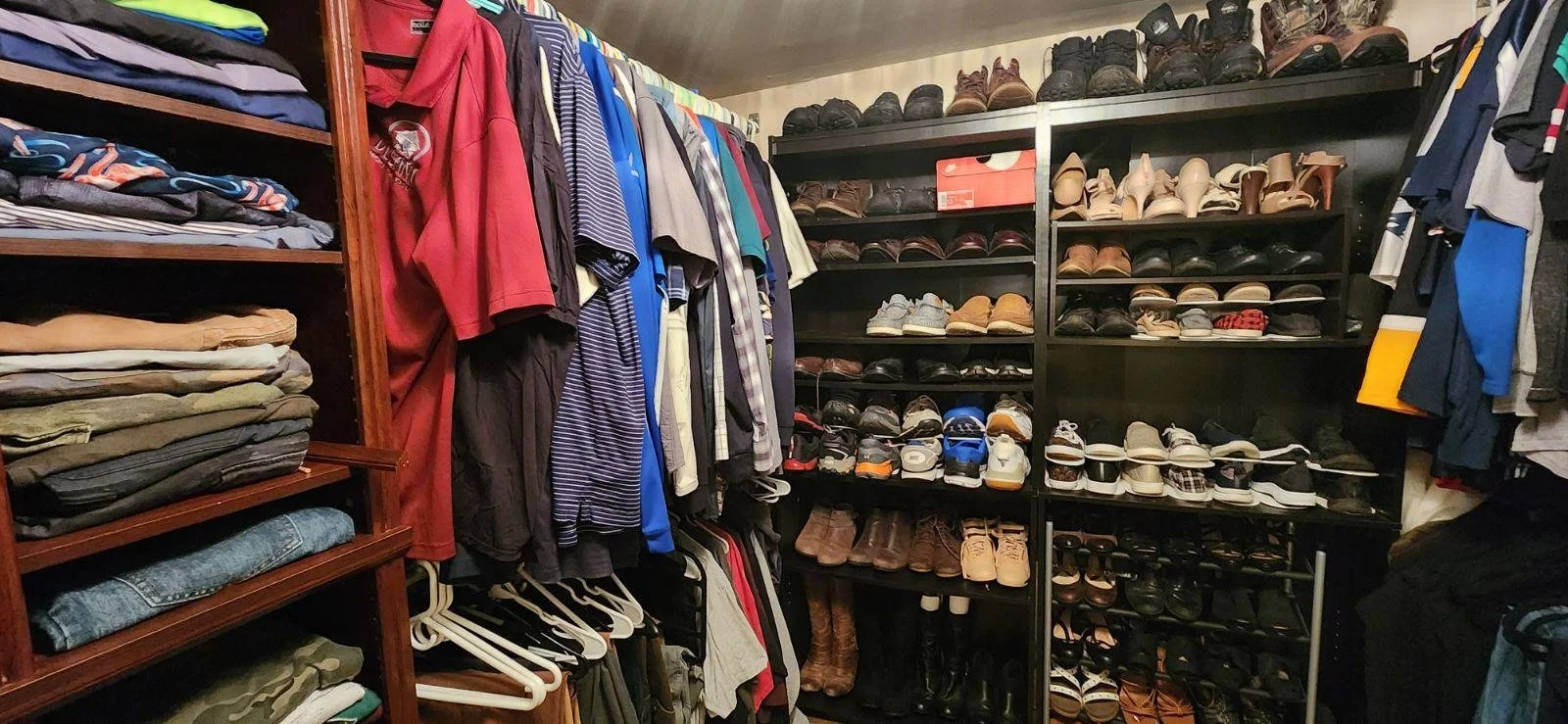 A walk-in closet with organized shelves of folded clothes, hanging shirts, and a large shoe collection on black shelves. Men's Primary Closet in Burlington, MA