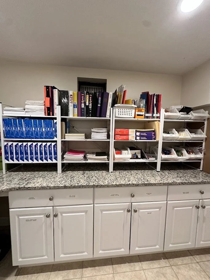 Kitchen counter with white cabinets below, granite countertop, and organized storage shelves above holding binders, papers, folders, and plastic storage containers.