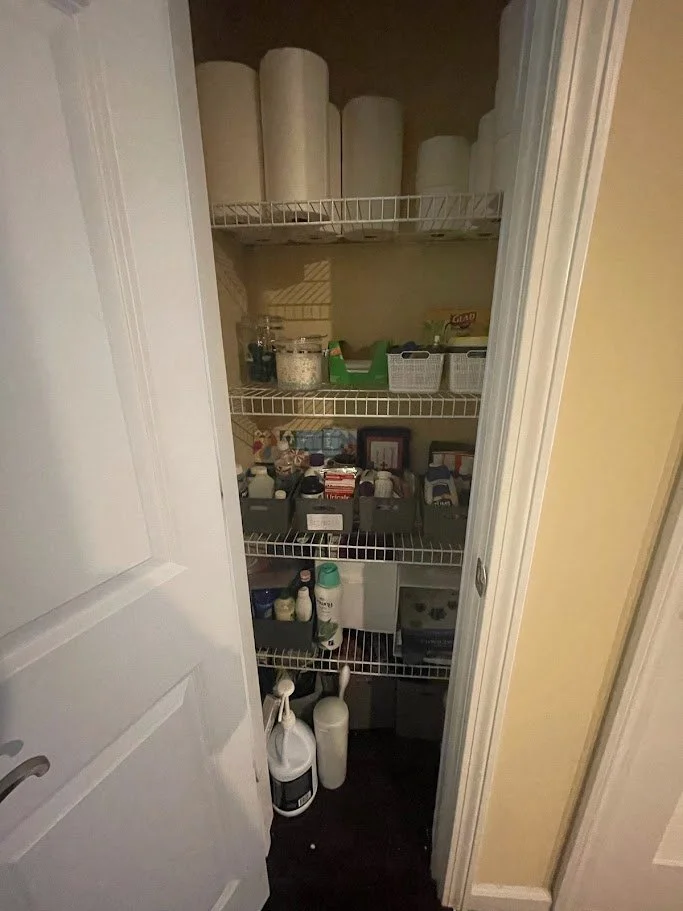 A small closet with wire shelves holding paper towels, storage containers, jars, and bottles of cleaning supplies.