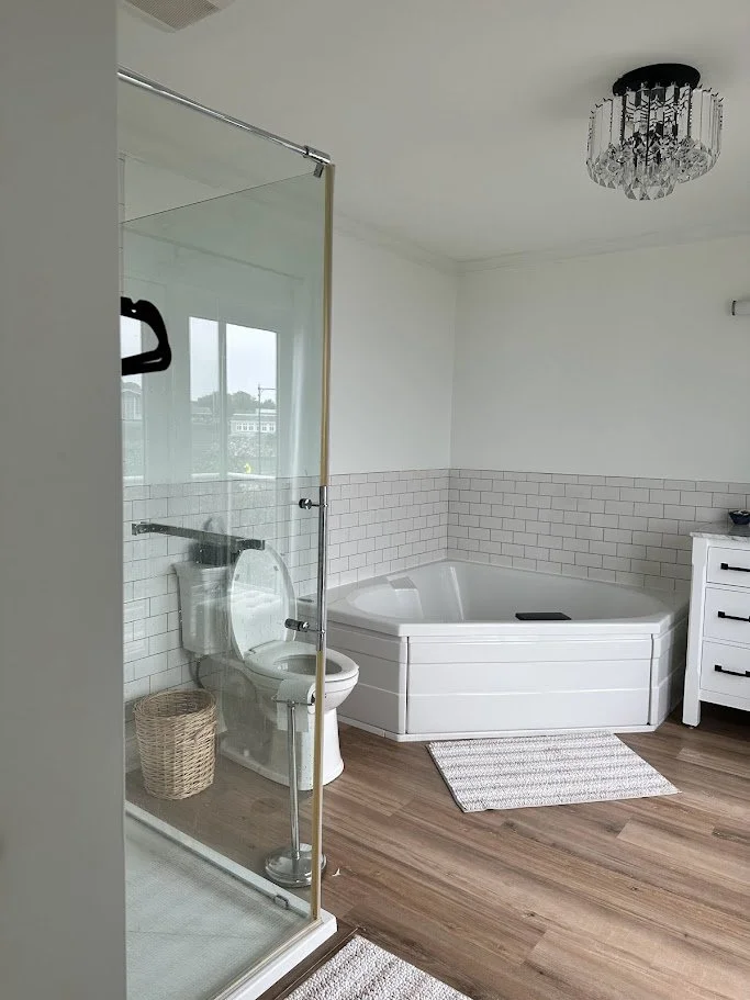 Bathroom with walk-in shower, toilet, and bathtub, with white walls, subway tile, and a wood floor.