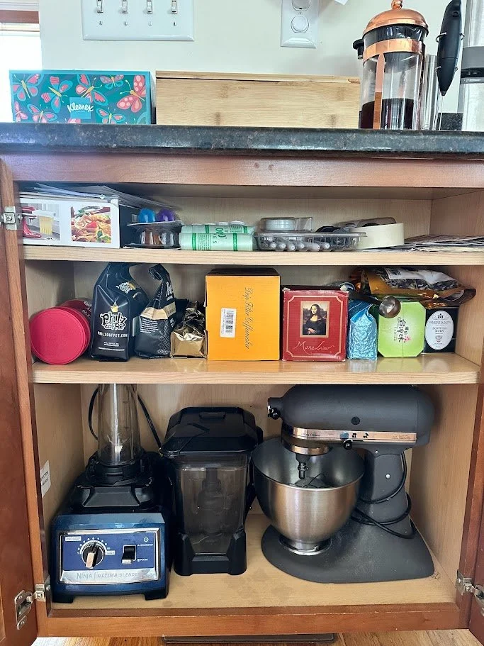 Kitchen cabinet with coffee brewing equipment, boxes of coffee, and various kitchen items on shelves.