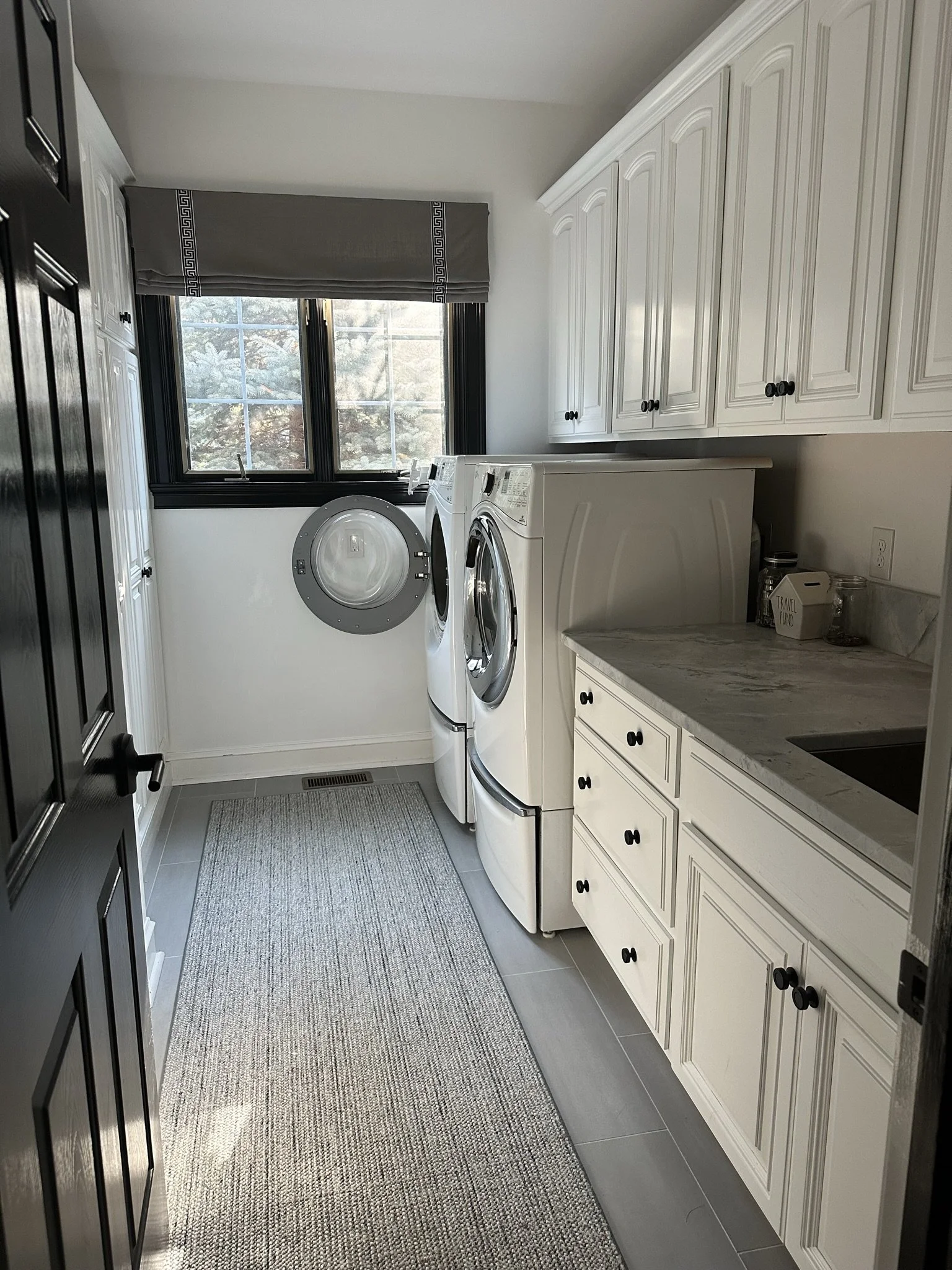 Laundry room with washer and dryer, white cabinets, countertop, gray rug, window with blinds.