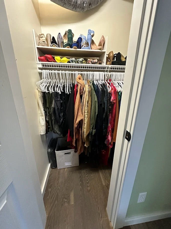 Closet with a shelf of shoes and a hanging rack of clothes, including jackets, shirts, and dresses, with a storage bin on the floor.