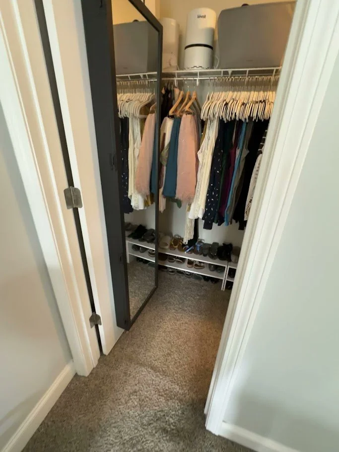 Inside a walk-in closet with hanging clothes, a mirror, and shoe shelves at the bottom.