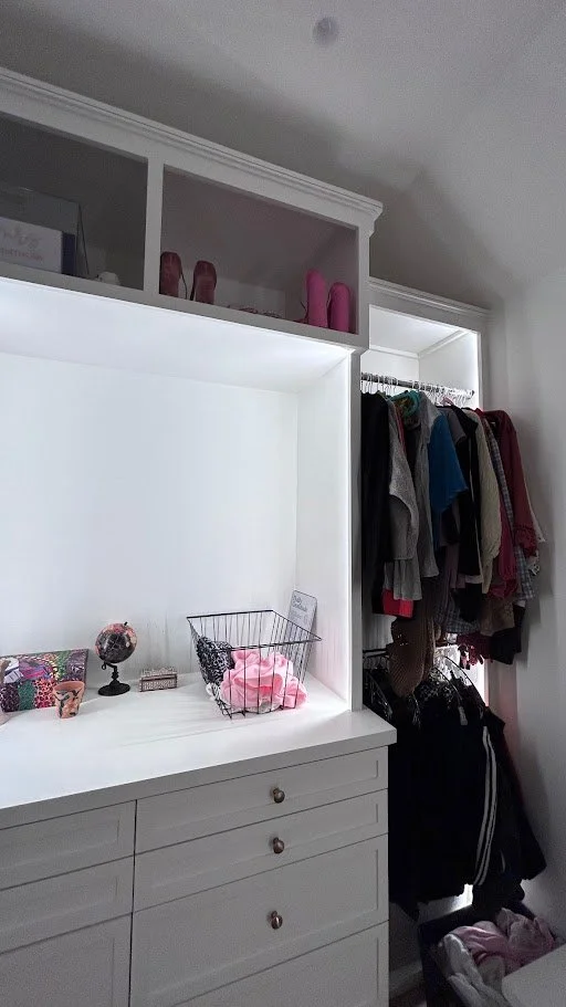 Part of a walk-in closet with white cabinetry, hanging clothes, and shelves with shoes and decorative items.