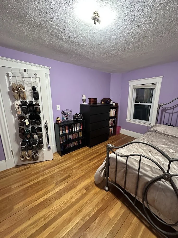 Bedroom with purple walls, a black metal bed, hardwood floor, a window, a dresser, and a shoe organizer on the door.