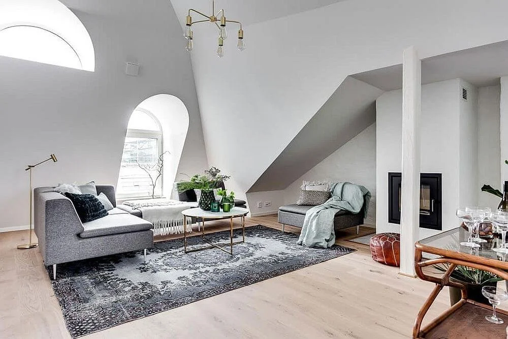 Modern living room with gray sofas, a black and white rug, a gold coffee table, and a fireplace, under a vaulted ceiling with large arched windows and a gold chandelier.