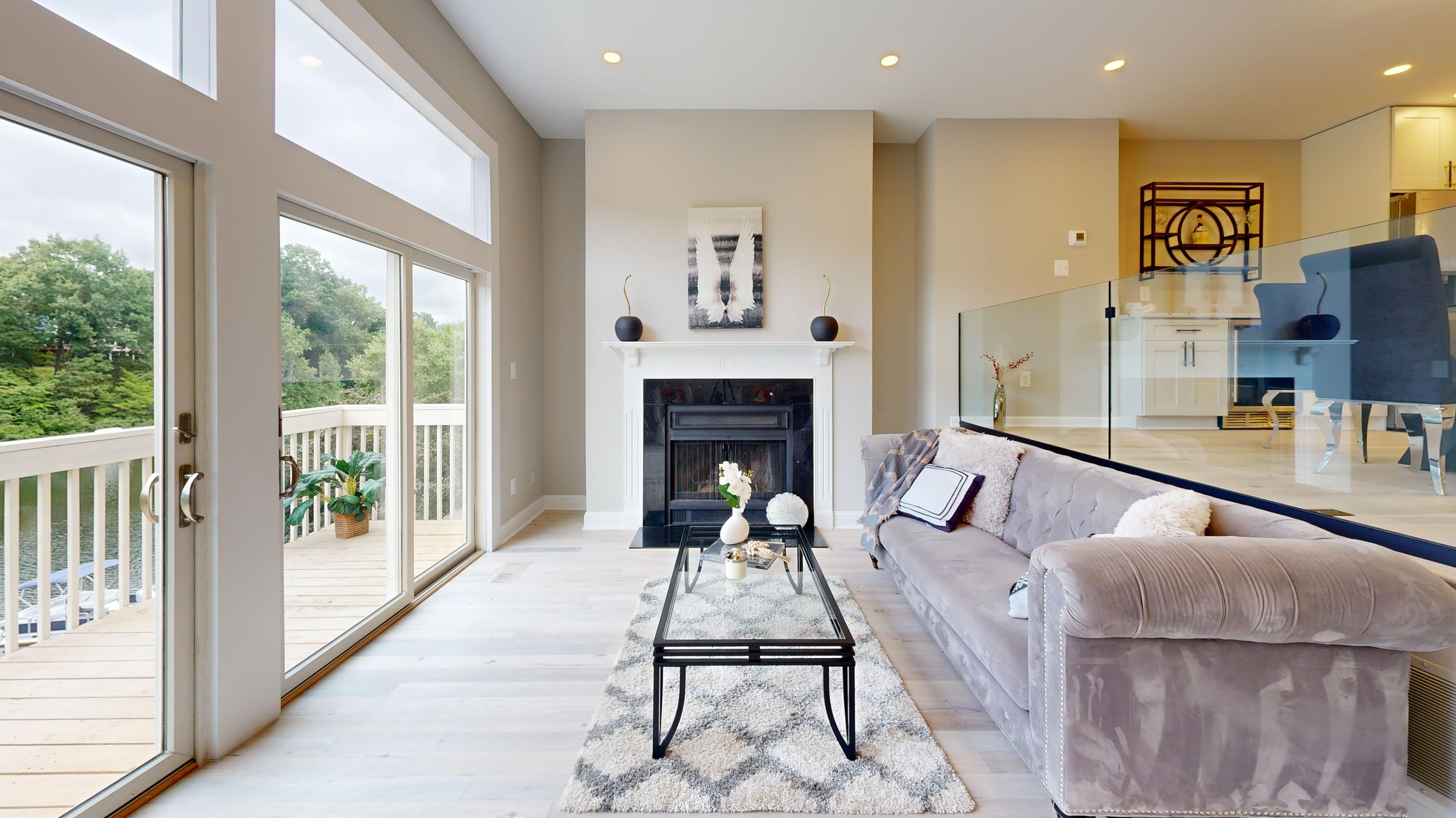 Living room with a balcony, fireplace, and modern decor, featuring a glass sliding door, plush sofa, coffee table, and artwork above the fireplace.