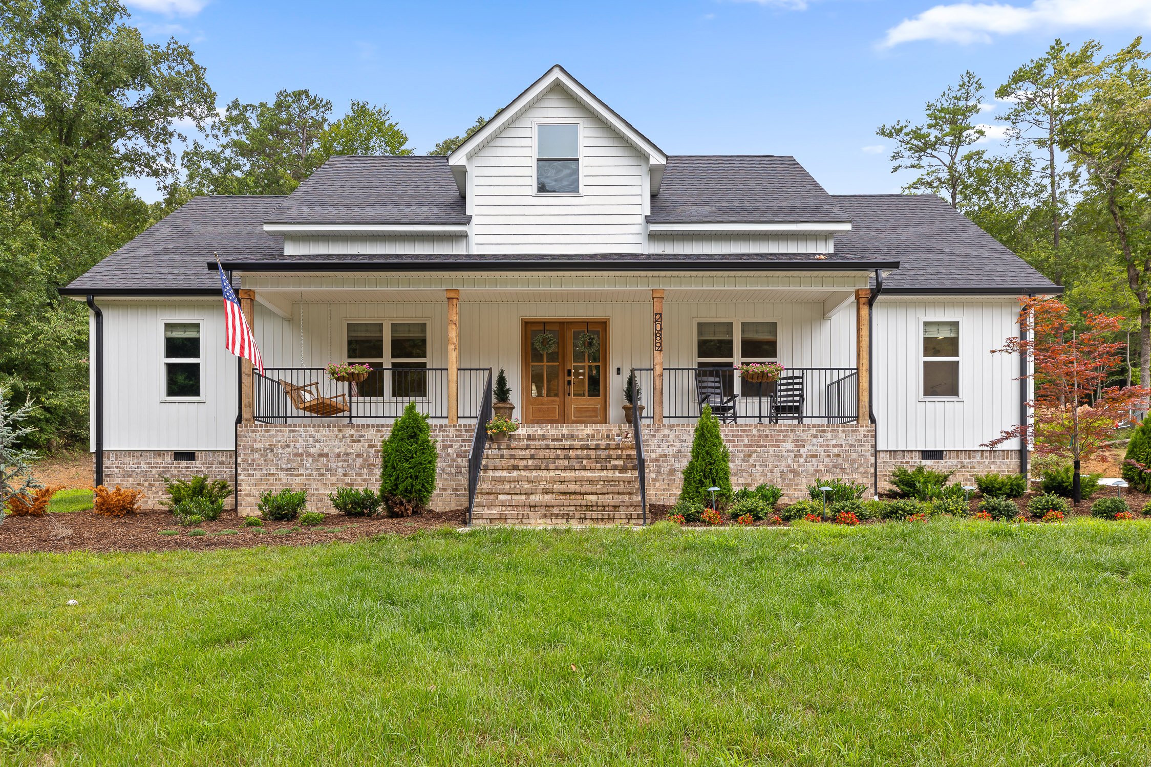 Front view of a white house with a porch, brick steps, and black railings, surrounded by green grass and trees.