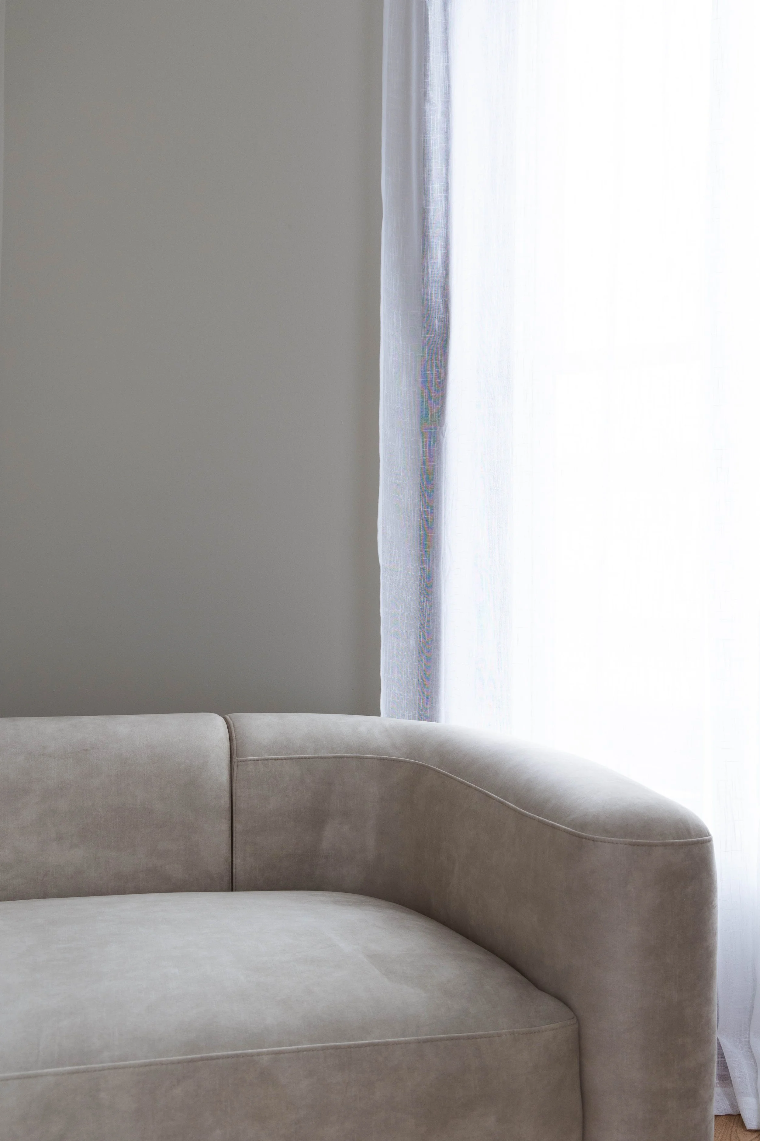 A beige sofa in front of a window with white sheer curtains at our Fort Collins, Colorado Boudoir Studio.